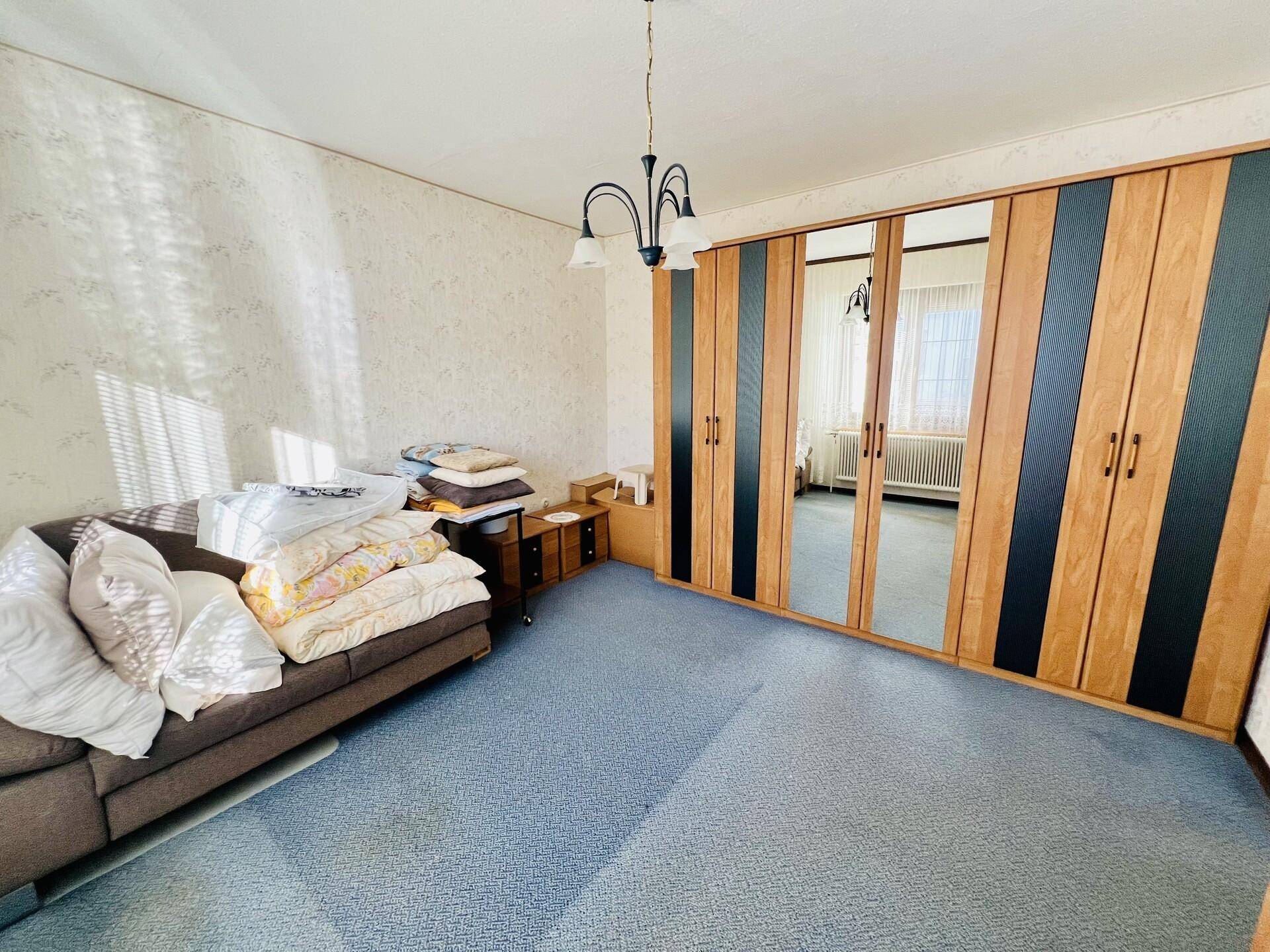 Schlafzimmer mit blauem Teppichboden und großem Spiegelschrank, der den Raum optisch erweitert.