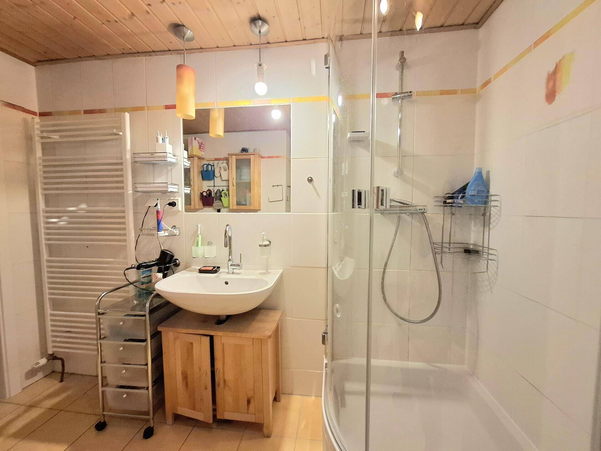 Badezimmer mit Waschbecken auf Holzunterschrank, Duschkabine und beheiztem Handtuchhalter.