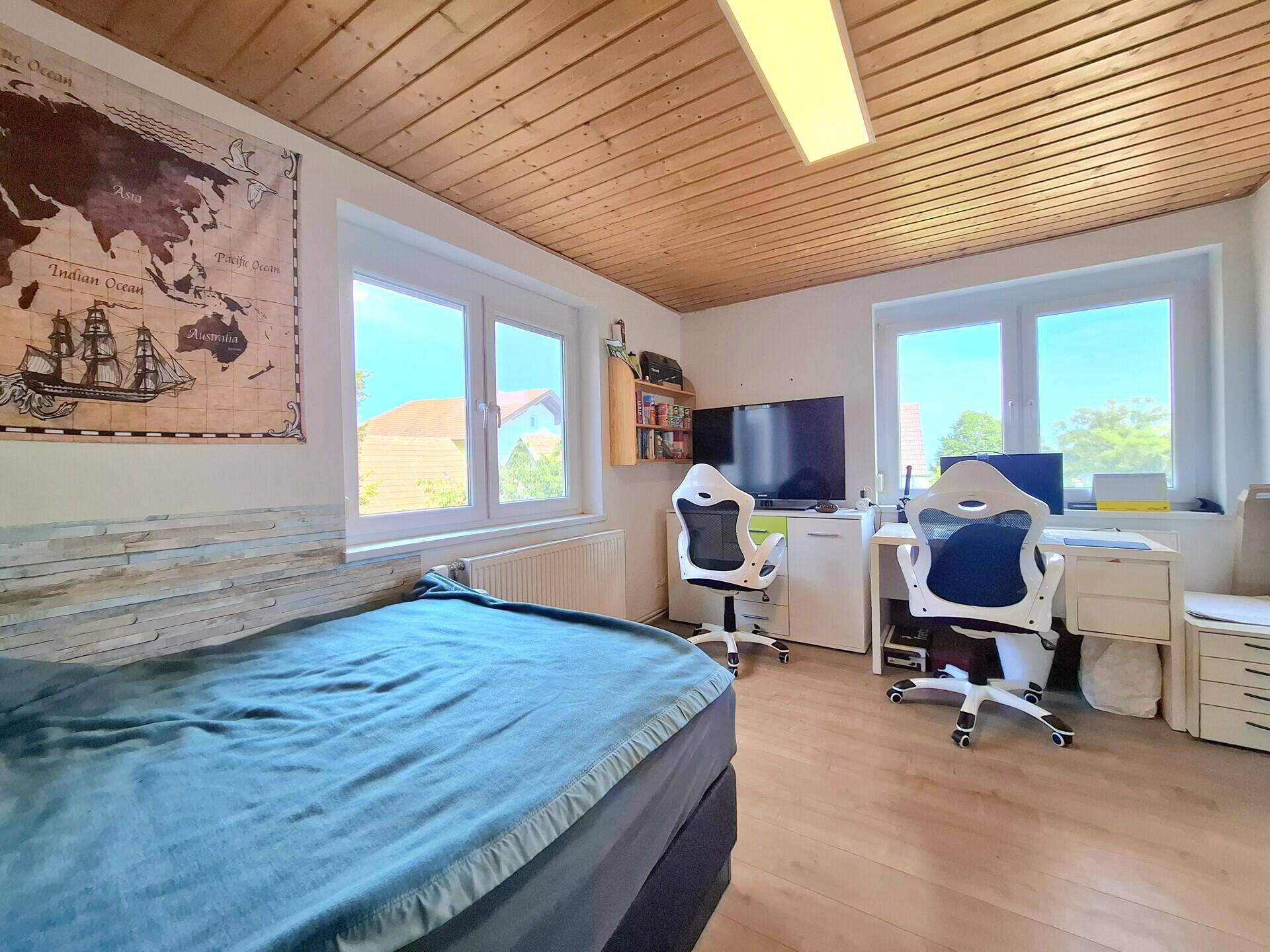Schlafzimmer mit Holzbalkendecke, zwei Schreibtischen und großzügigen Fenstern für viel Tageslicht.
