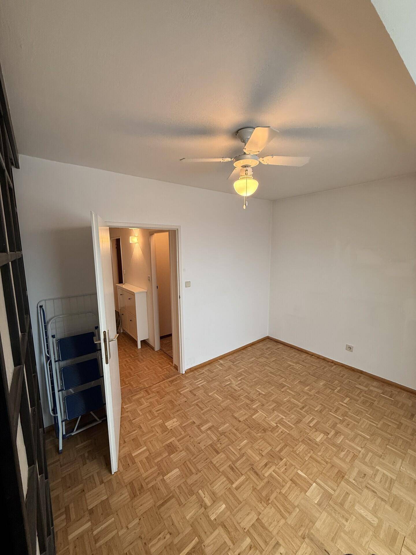 Geräumiges Schlafzimmer mit Parkettboden und Deckenventilator, Blick zum Flur.