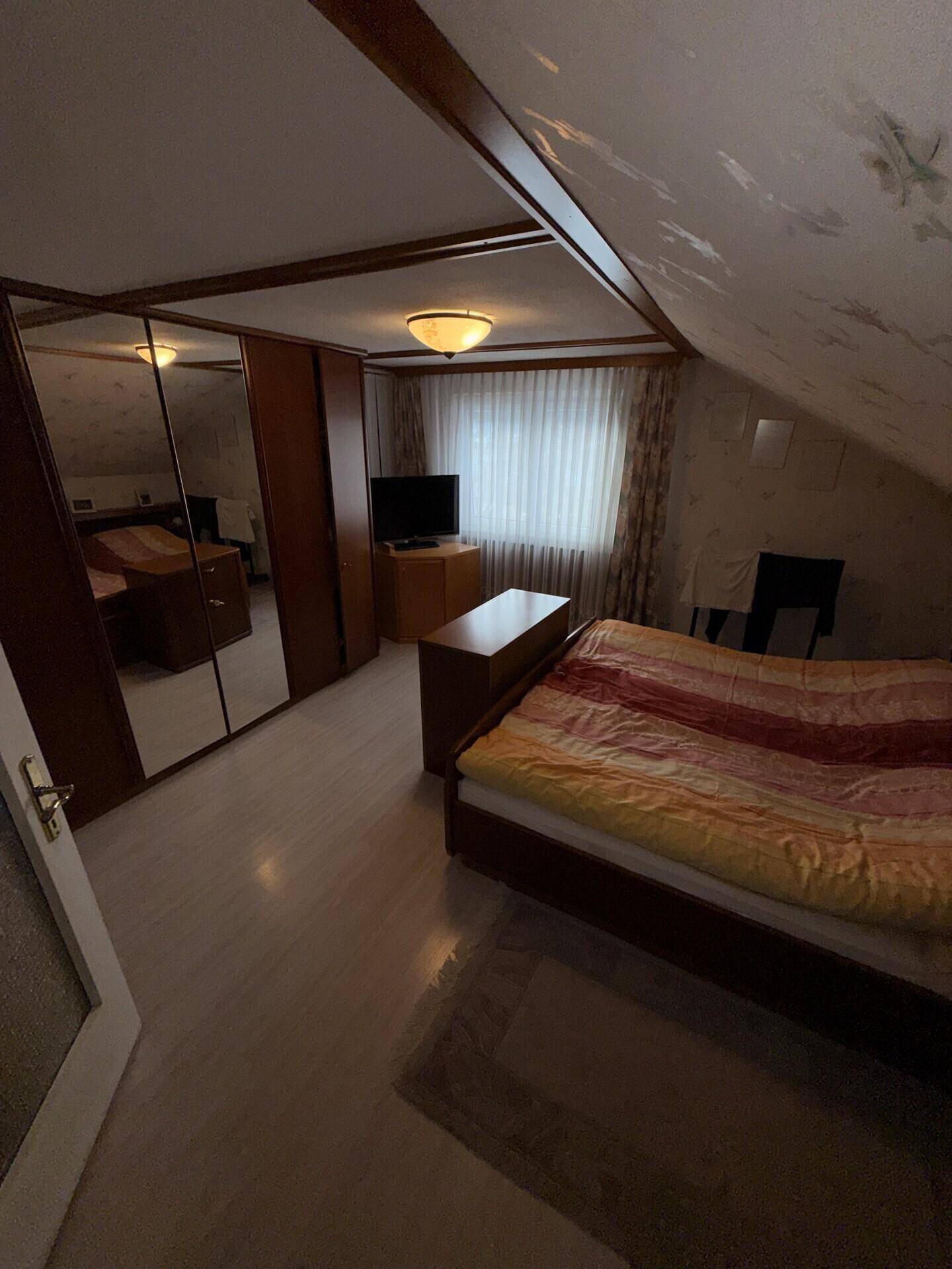 Dachgeschoss-Schlafzimmer mit Dachschrägen, Holzverkleidung und Bett in gemütlichem Ambiente.