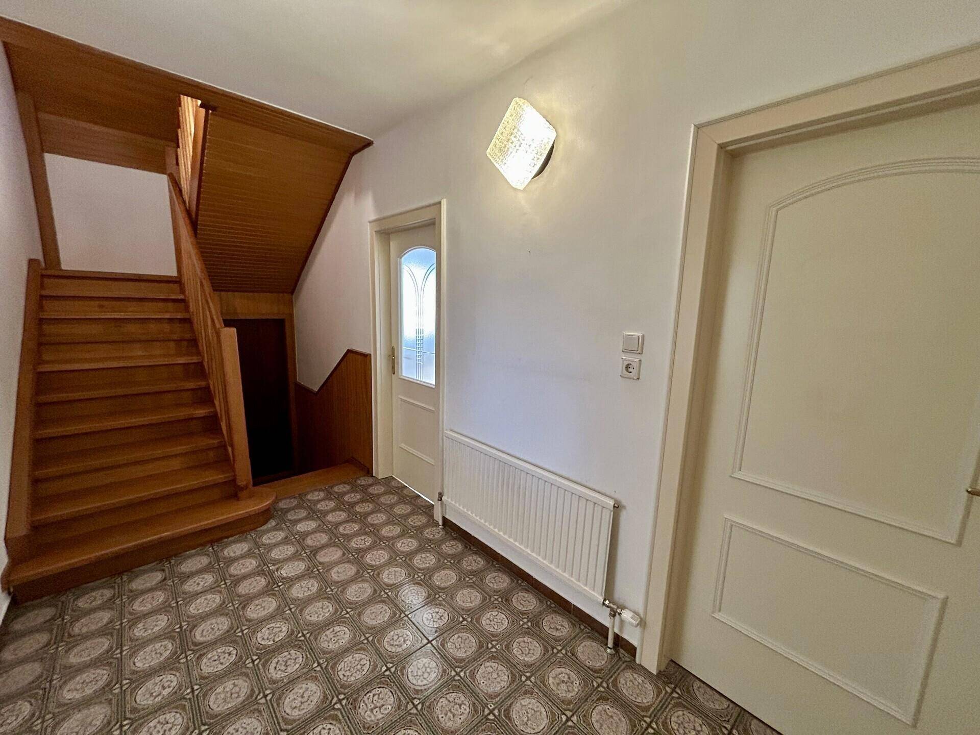 Geräumiger Flur mit Holztreppe, gemustertem Boden und Zugang zu weiteren Räumen.