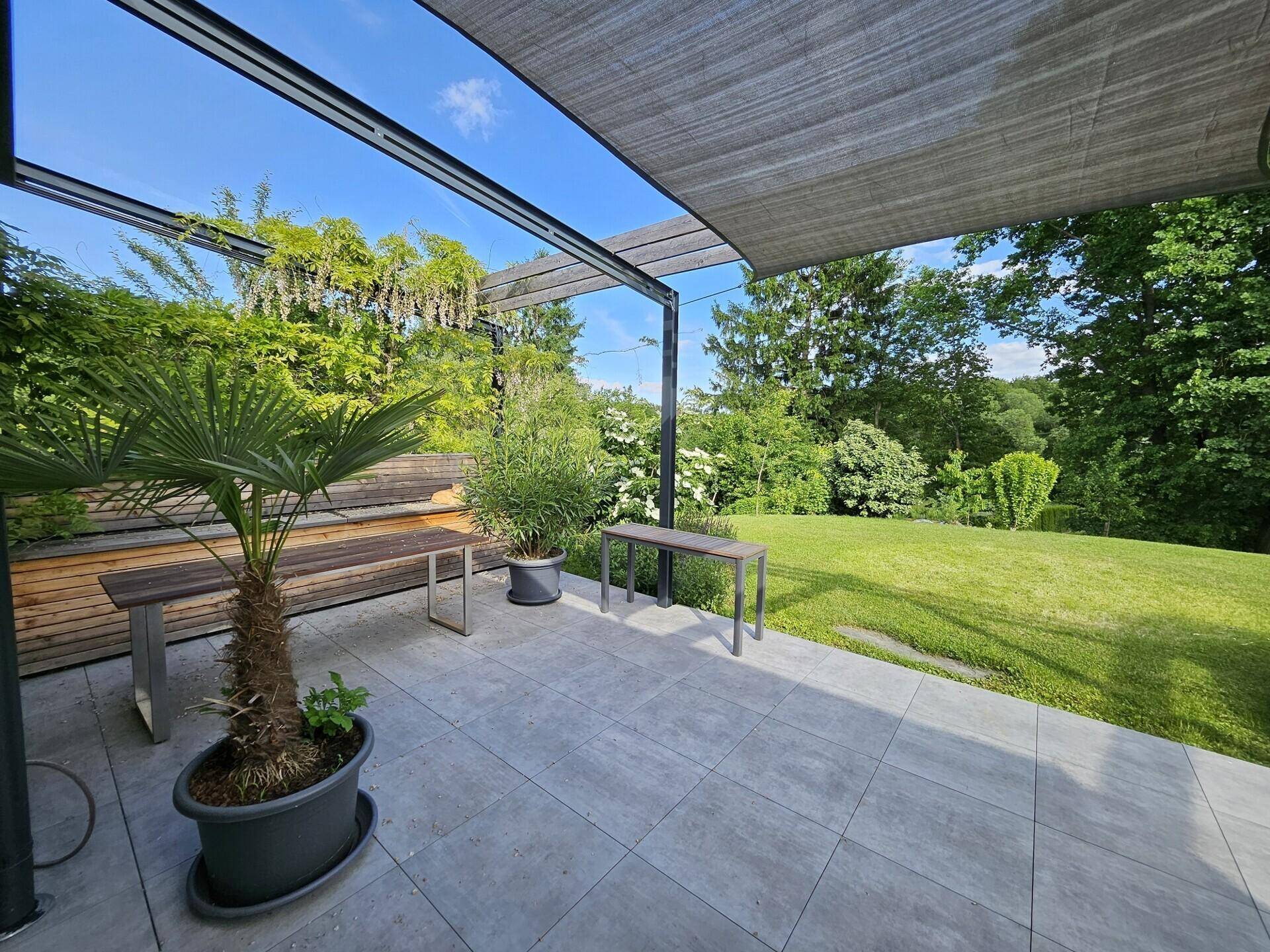 Sonniger Terrassenbereich mit Pergola, bequemen Sitzgelegenheiten und Blick auf den Garten.