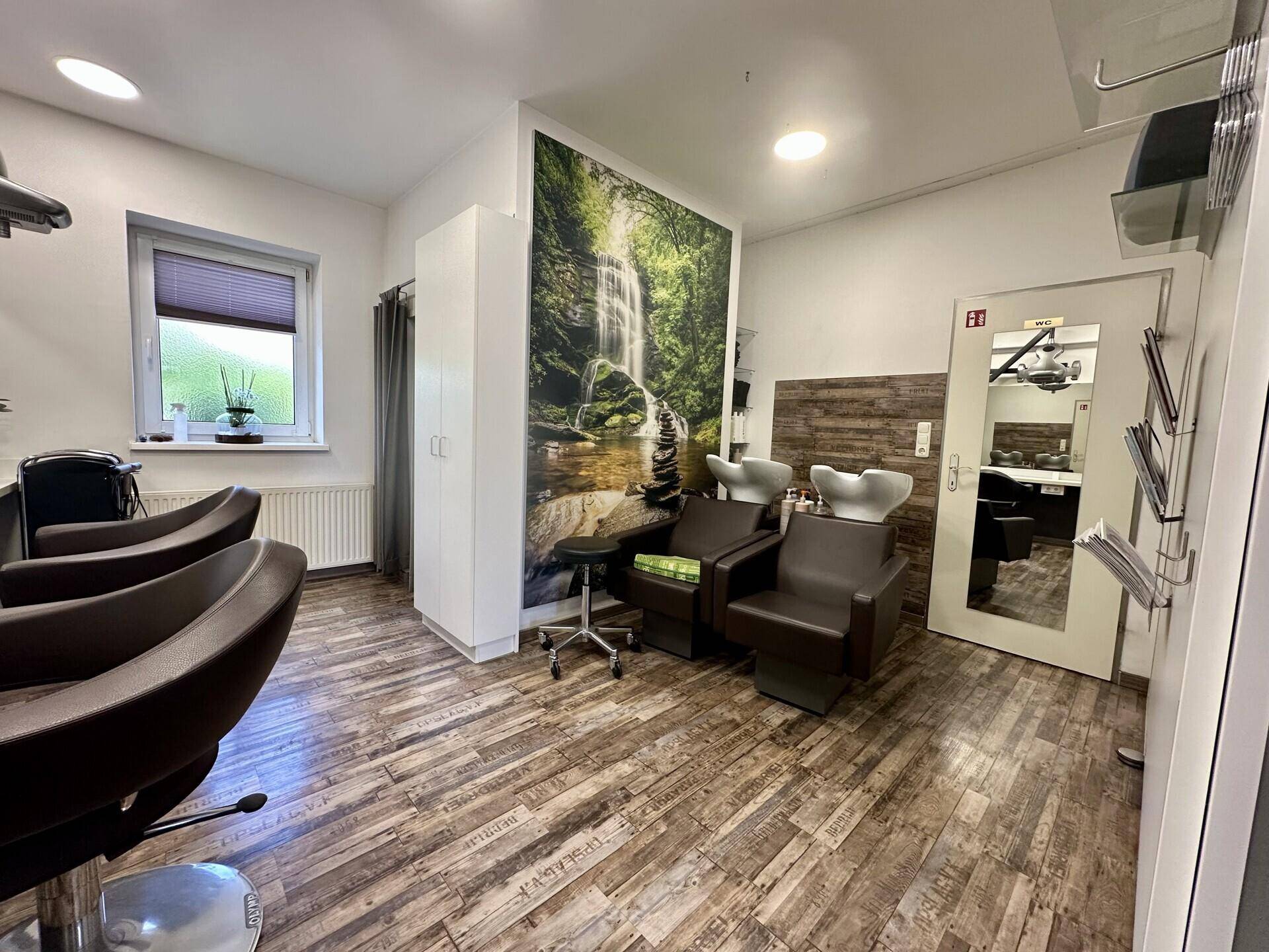 Helle Waschbecken im Friseursalon mit Fenster und dekorativer Wandtapete mit Wasserfallmotiv.