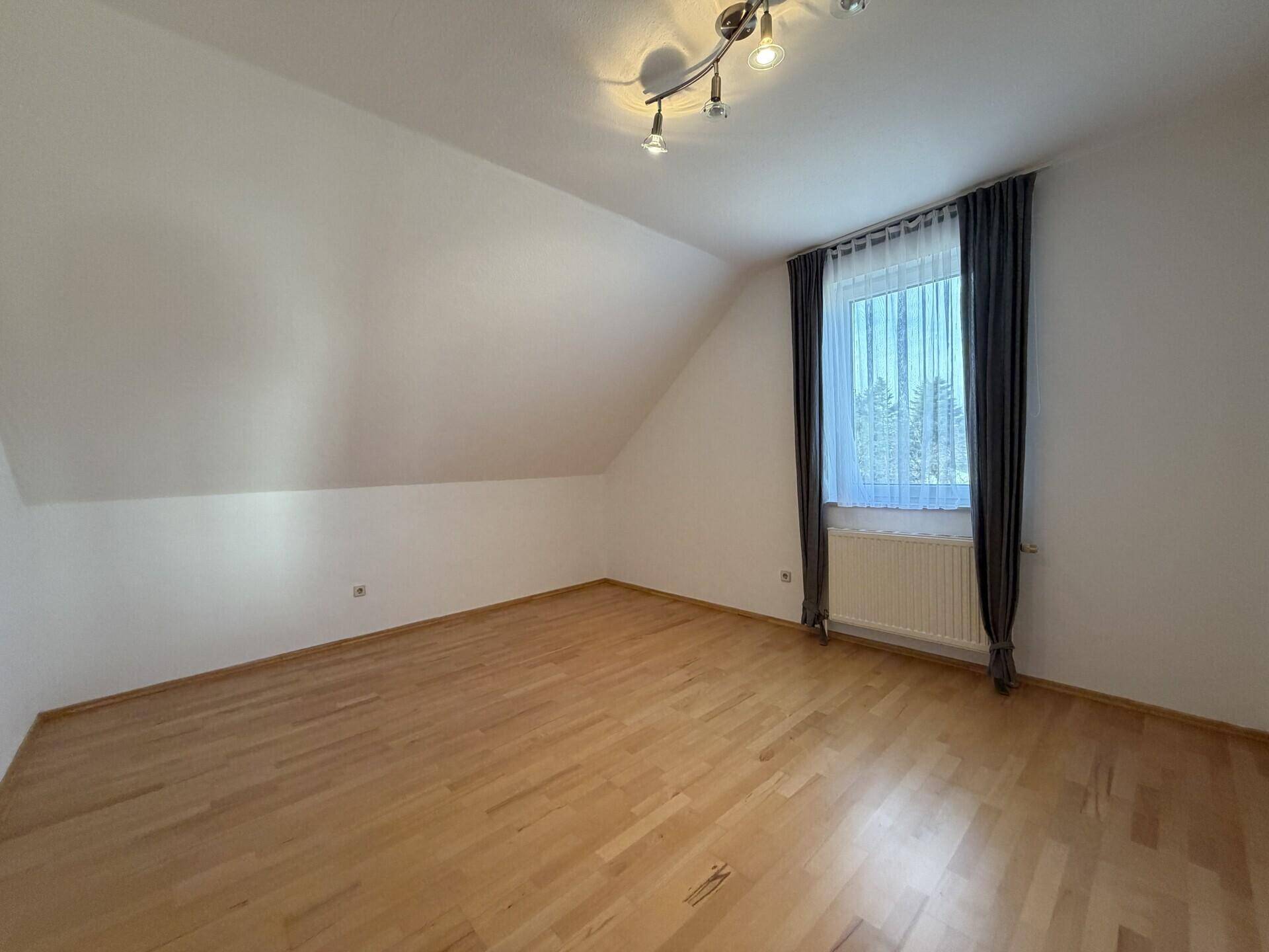 Helles Schlafzimmer im Dachgeschoss mit Parkettboden, Dachschräge und Fenster.