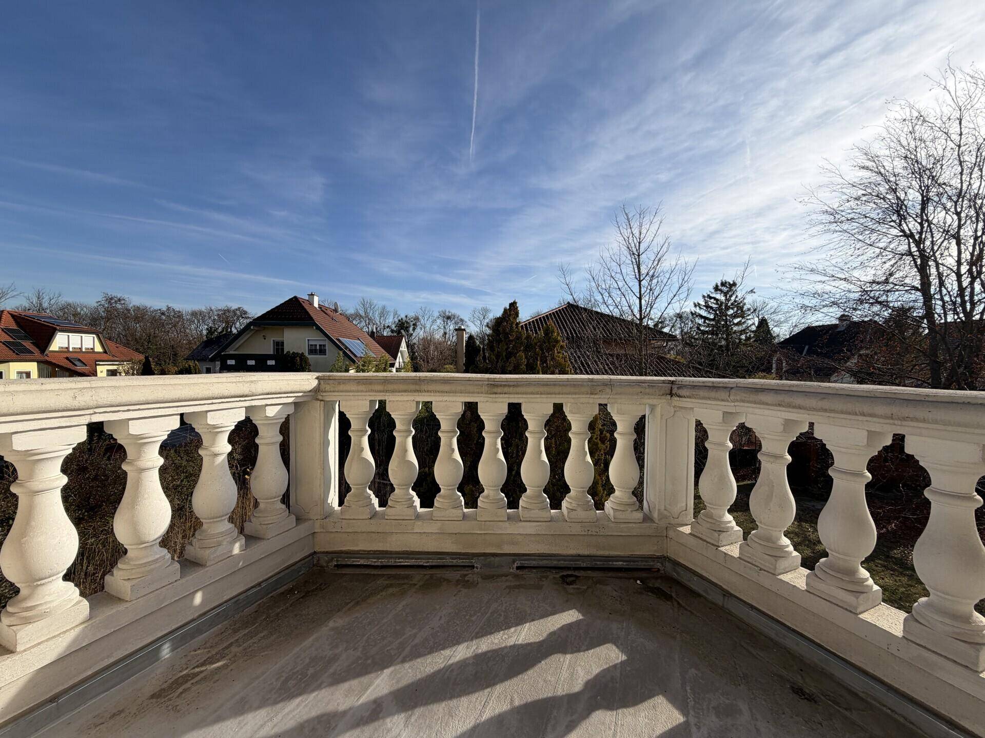 Klassischer Balkon mit Balustrade und weitem Blick über die Nachbarschaft unter blauem Himmel.