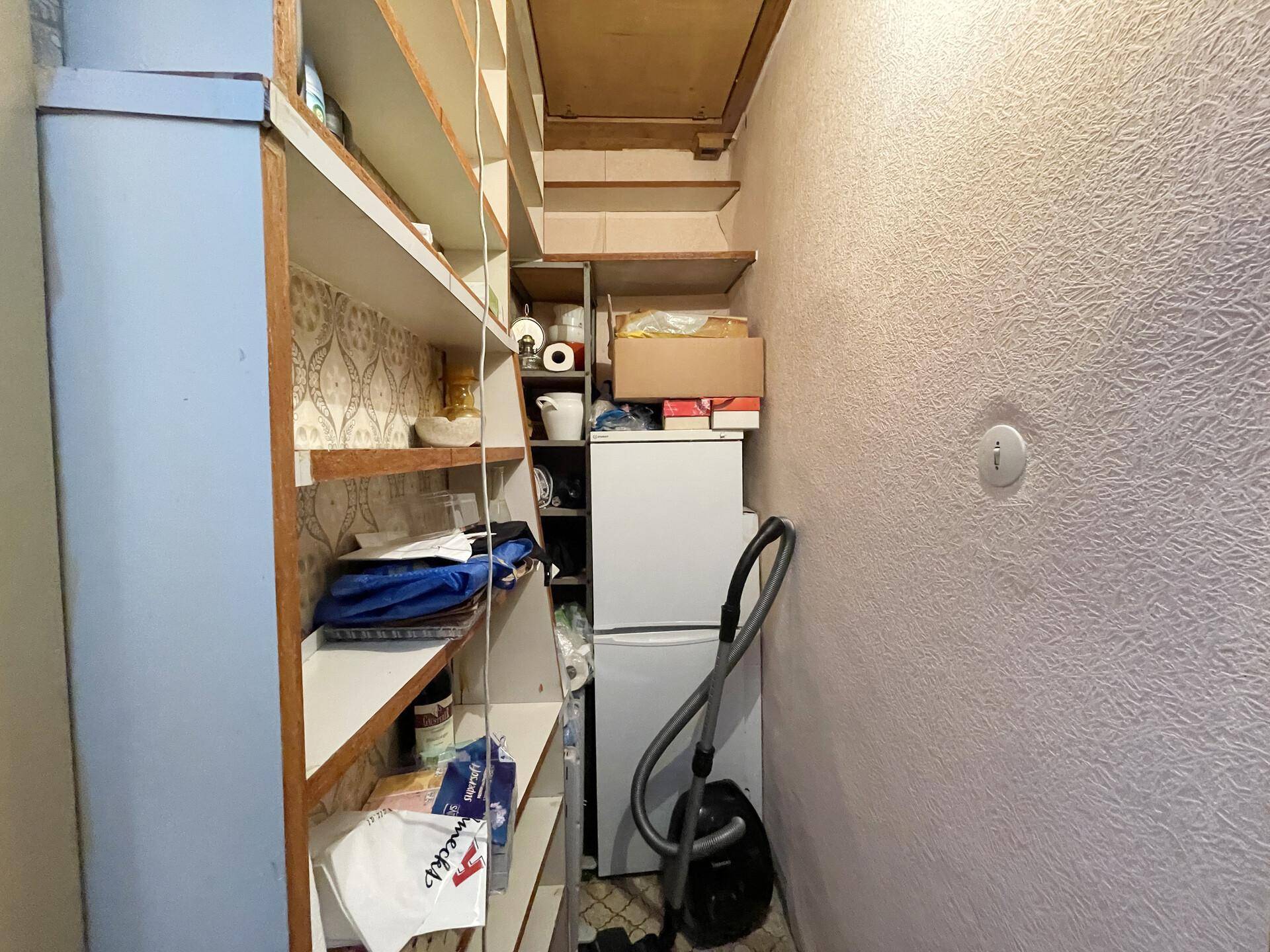 Kleiner Abstellraum mit Regalen, Kühlschrank und Staubsauger für Haushaltsgeräte.
