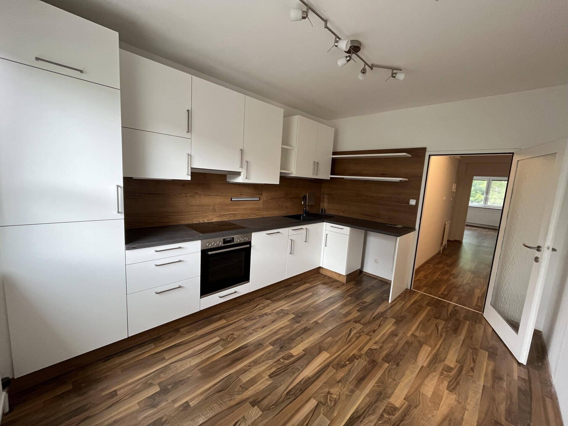 Moderne Einbauküche in L-Form mit weißen Schränken und Holzoptik-Rückwand.