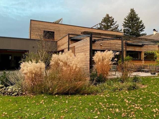 Modernes Wohnhaus mit Holzfassade und herbstlicher Gartengestaltung unter bewölktem Himmel.