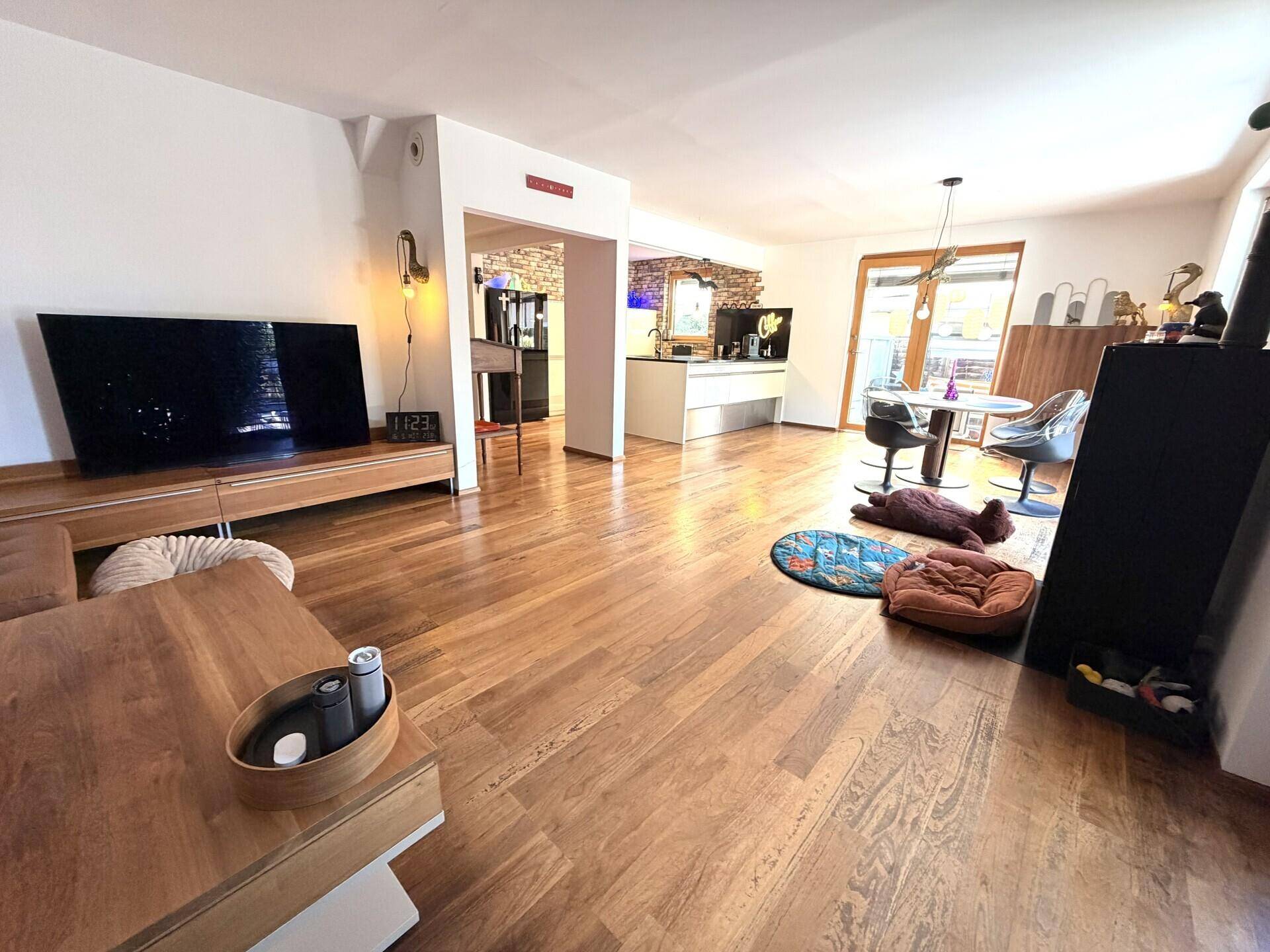 Geräumiger Wohnbereich mit Holzboden, großem Fernseher und offenem Zugang zur Küche.