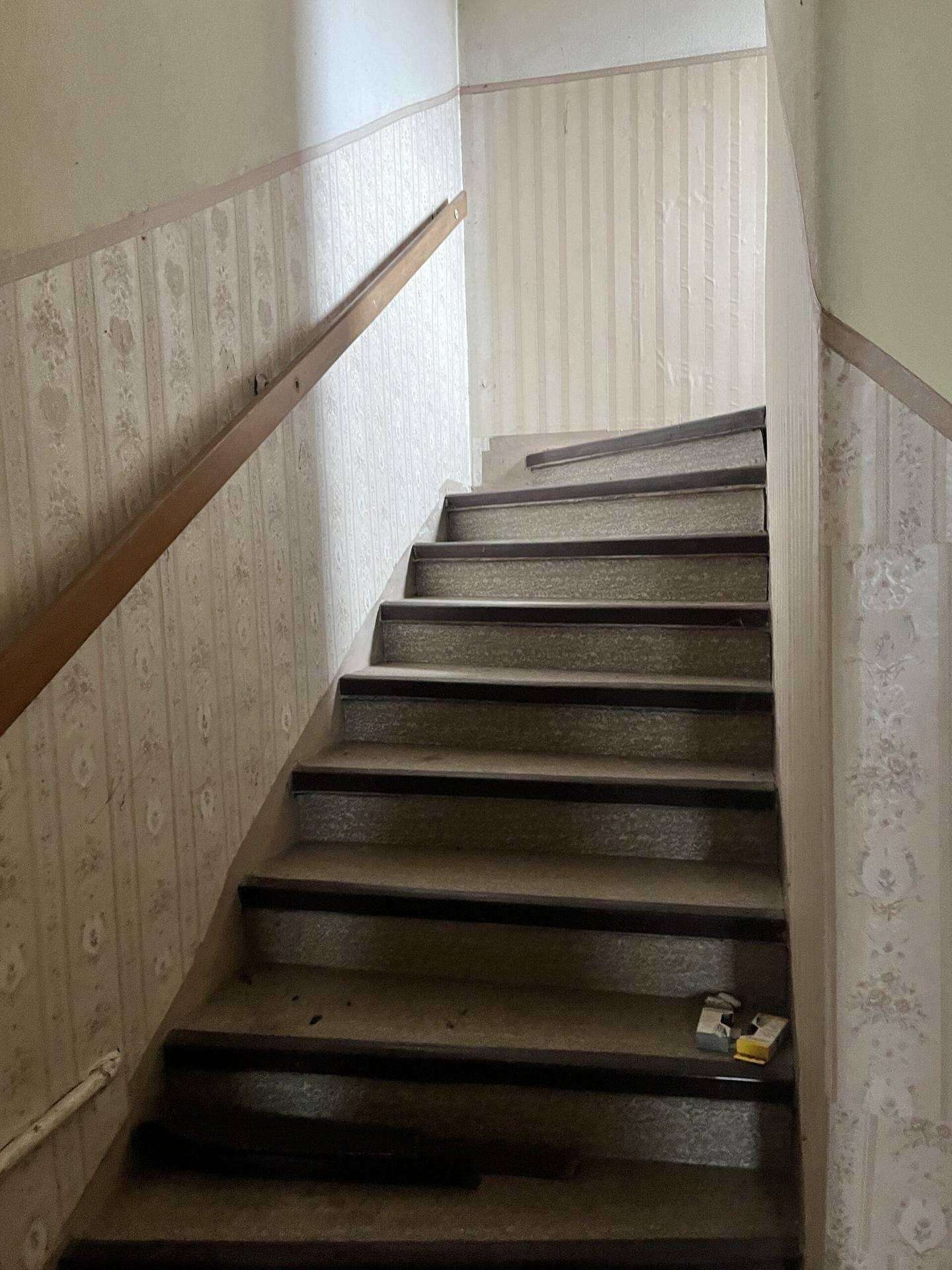 Treppenhaus mit Holzgeländer und gemusterter Tapete, das die Etagen verbindet.