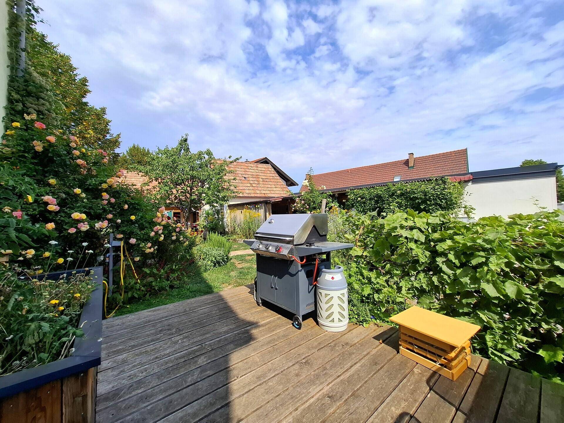 Geräumige Holzterrasse mit Grill und Blick auf den grünen Gartenbereich.
