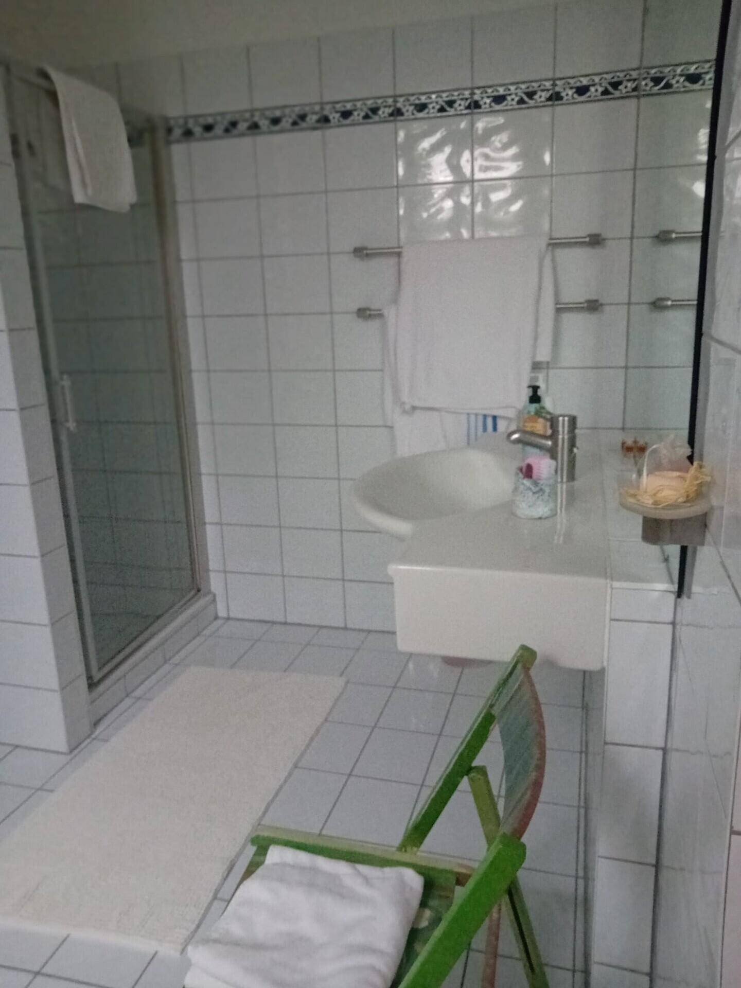 Badezimmer mit Duschkabine, Waschbecken und weißen Fliesen, schlichtes Design.