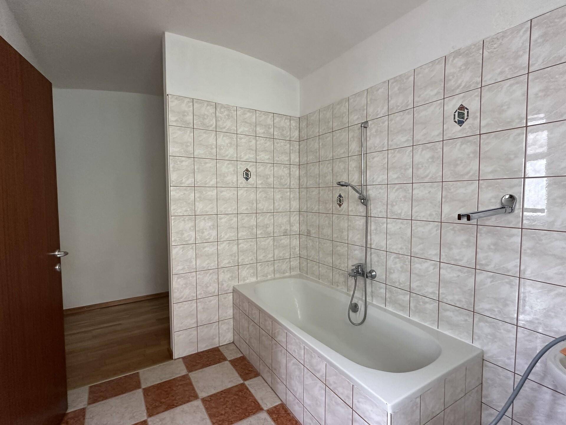 Badezimmer mit Badewanne und hellen Fliesen, bereit für eine Modernisierung im 80er-Jahre-Stil.