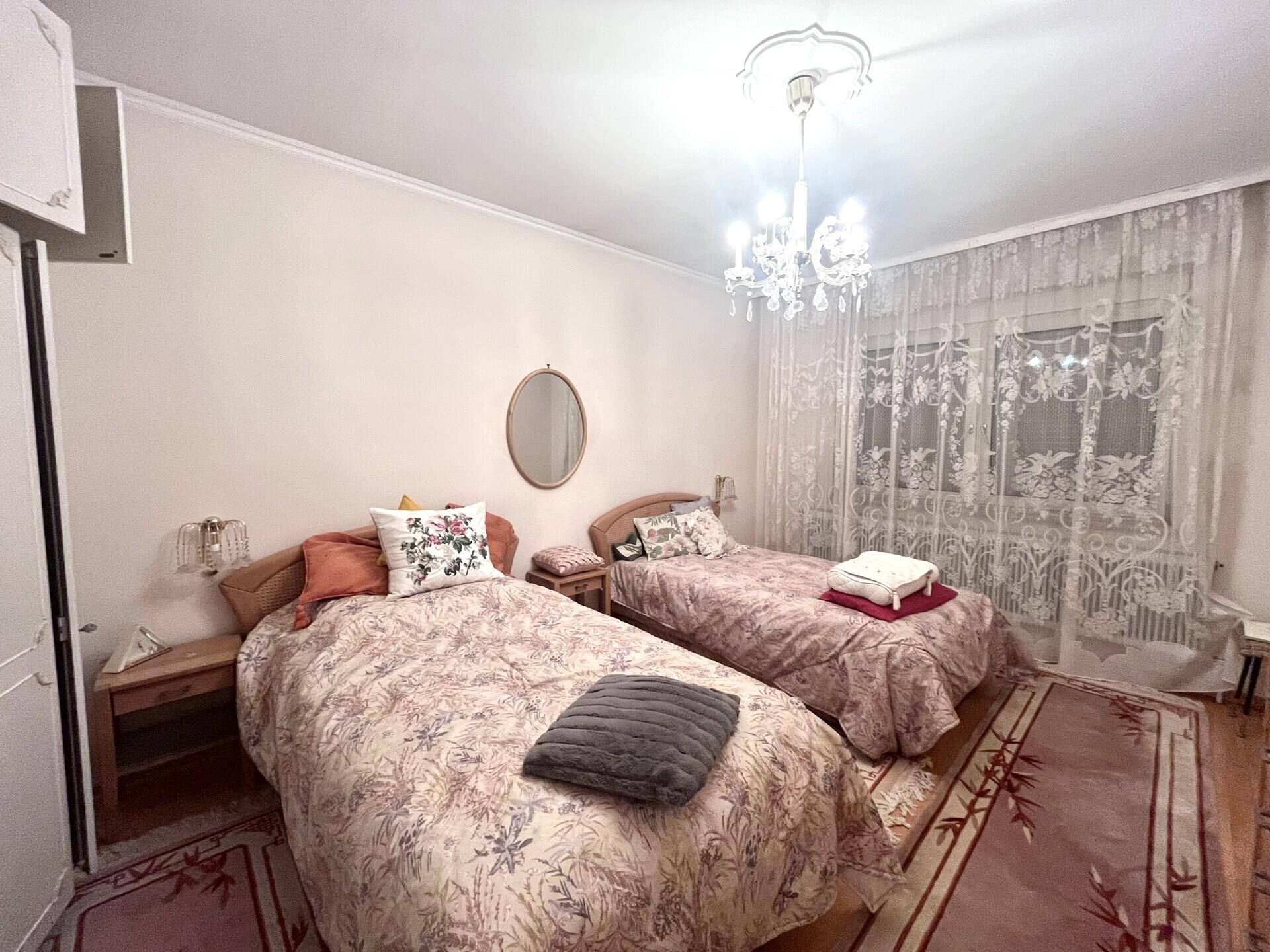 Schlafzimmer mit zwei Einzelbetten, elegantem Kronleuchter und gemusterten Vorhängen am Fenster.