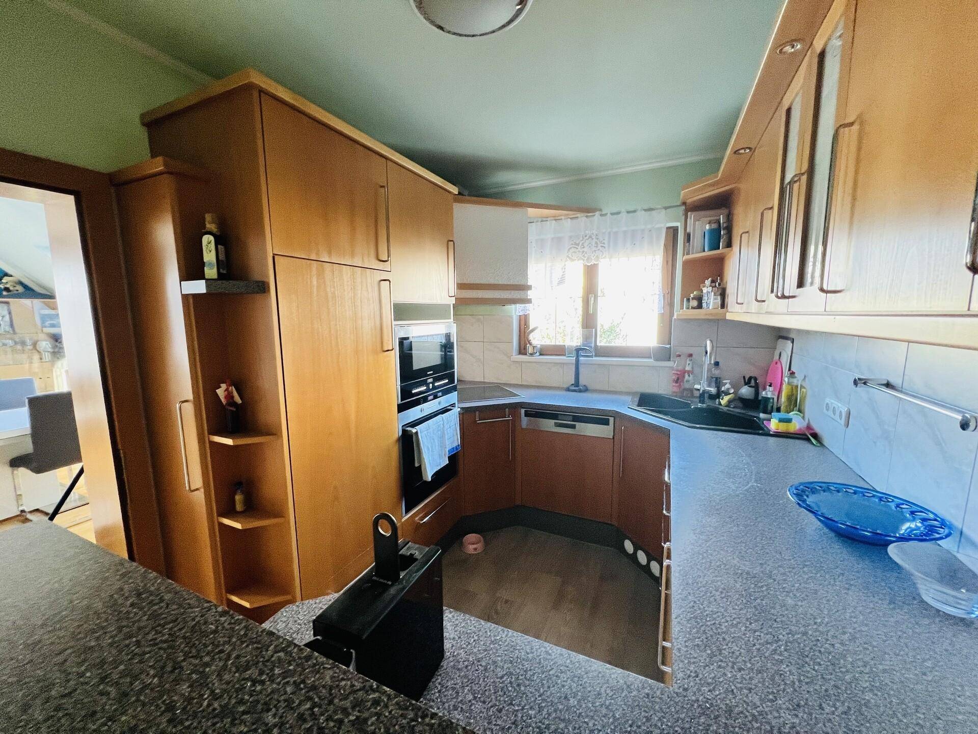 Funktionale Küche mit Holzschränken, dunkler Arbeitsplatte und Einbaugeräten.