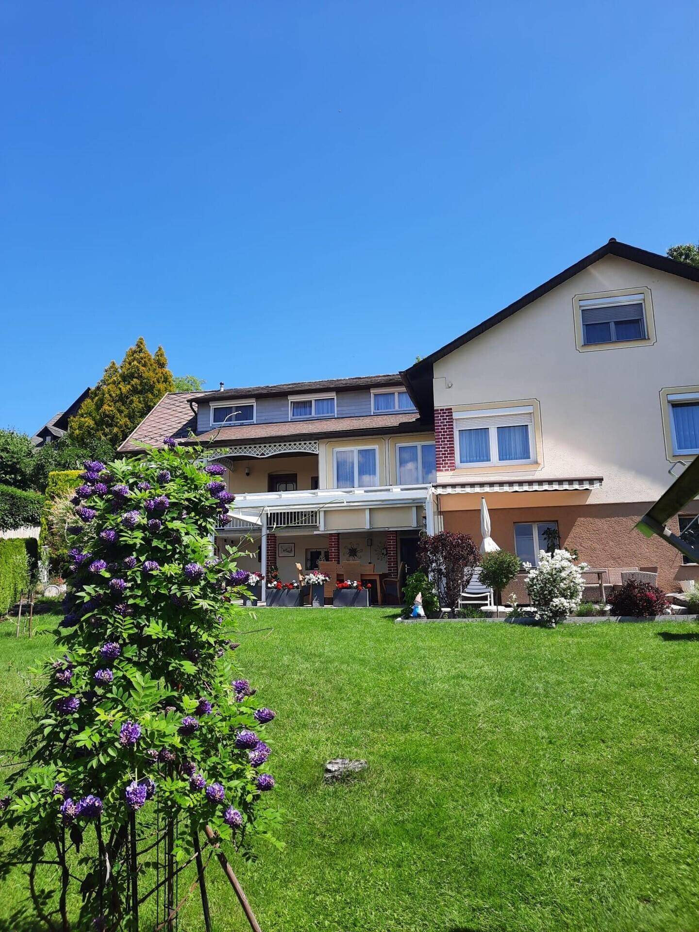 Weitläufiger Garten mit Rasenfläche und Blick auf die überdachte Terrasse des Hauses.