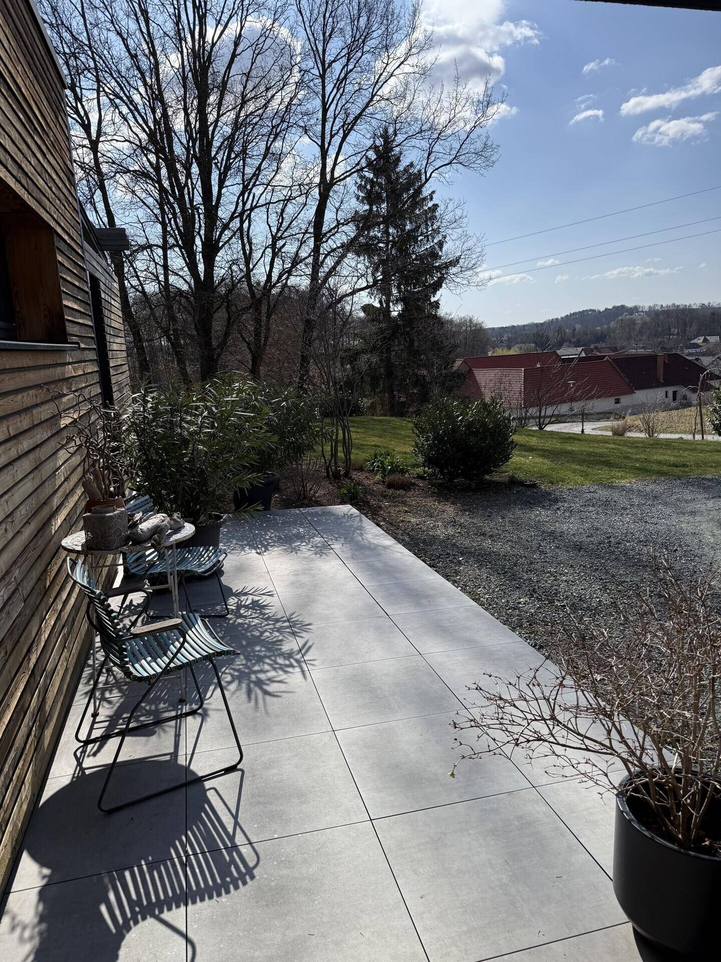 Gemütliche Terrasse mit Outdoor-Möbeln und Blick auf die grüne Umgebung unter blauem Himmel.