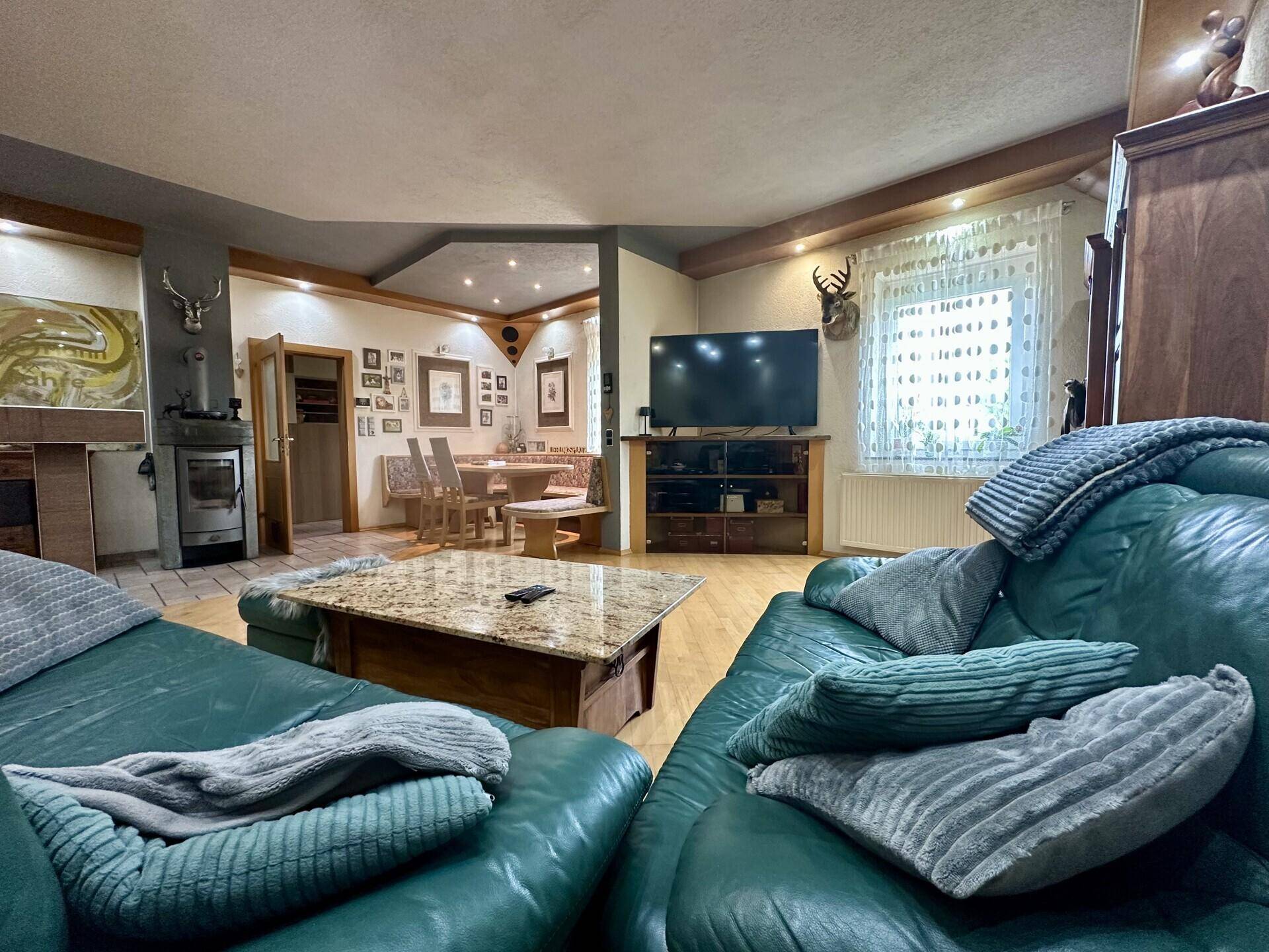 Gemütliches Wohnzimmer mit grünen Ledersofas, Couchtisch und einem traditionellen Kachelofen.