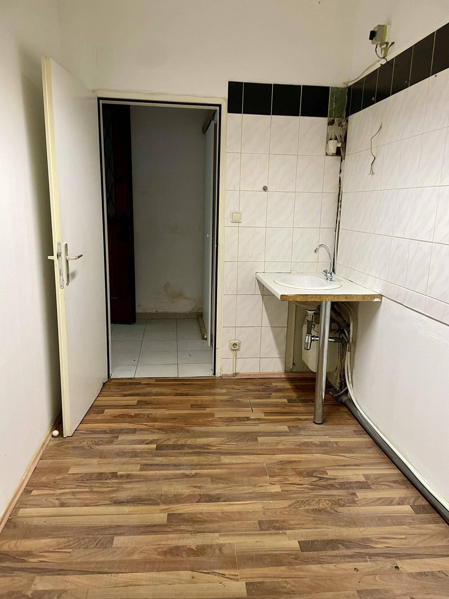 Kleiner Raum mit Holzboden, Waschbecken und gefliesten Wänden, bereit für weitere Einrichtung.