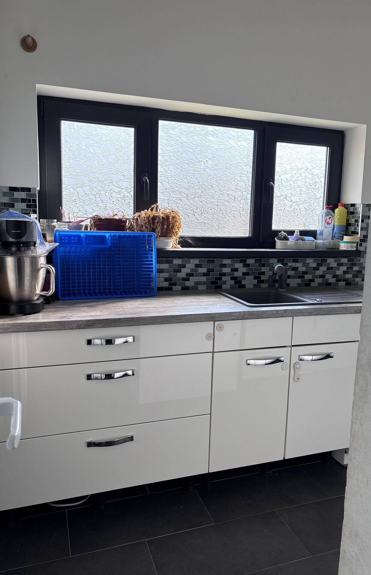 Moderne Küche mit weißen Hochglanzschränken, dunkler Arbeitsplatte und Fenster.