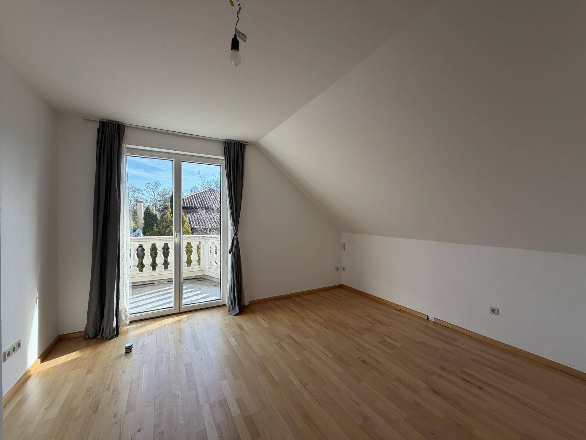 Schlafzimmer im Dachgeschoss mit Parkettboden, Dachschräge und Zugang zu einem Balkon.