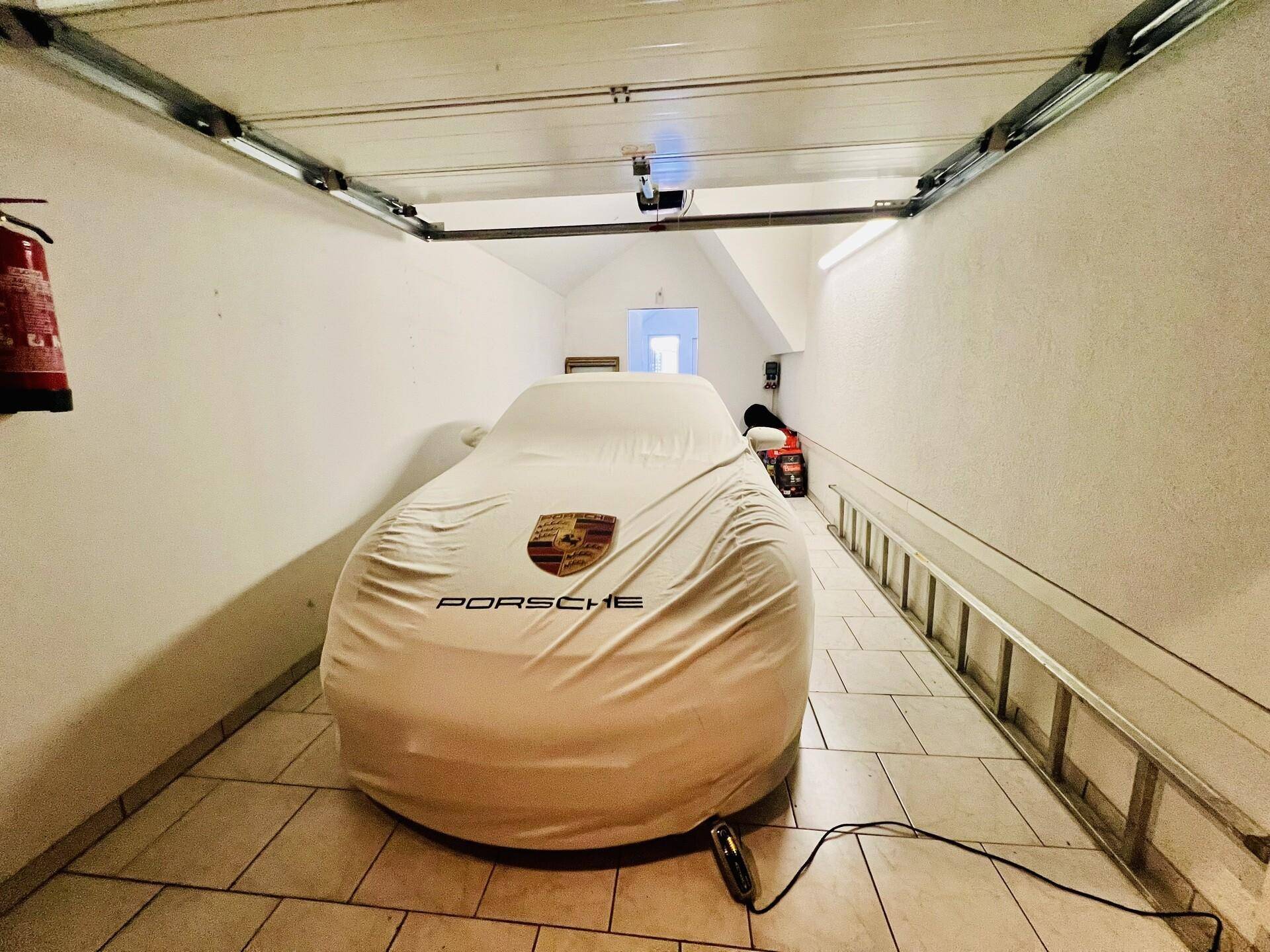 Geräumige Garage mit Fliesenboden und einem abgedeckten Fahrzeug, bietet sicheren Stellplatz.