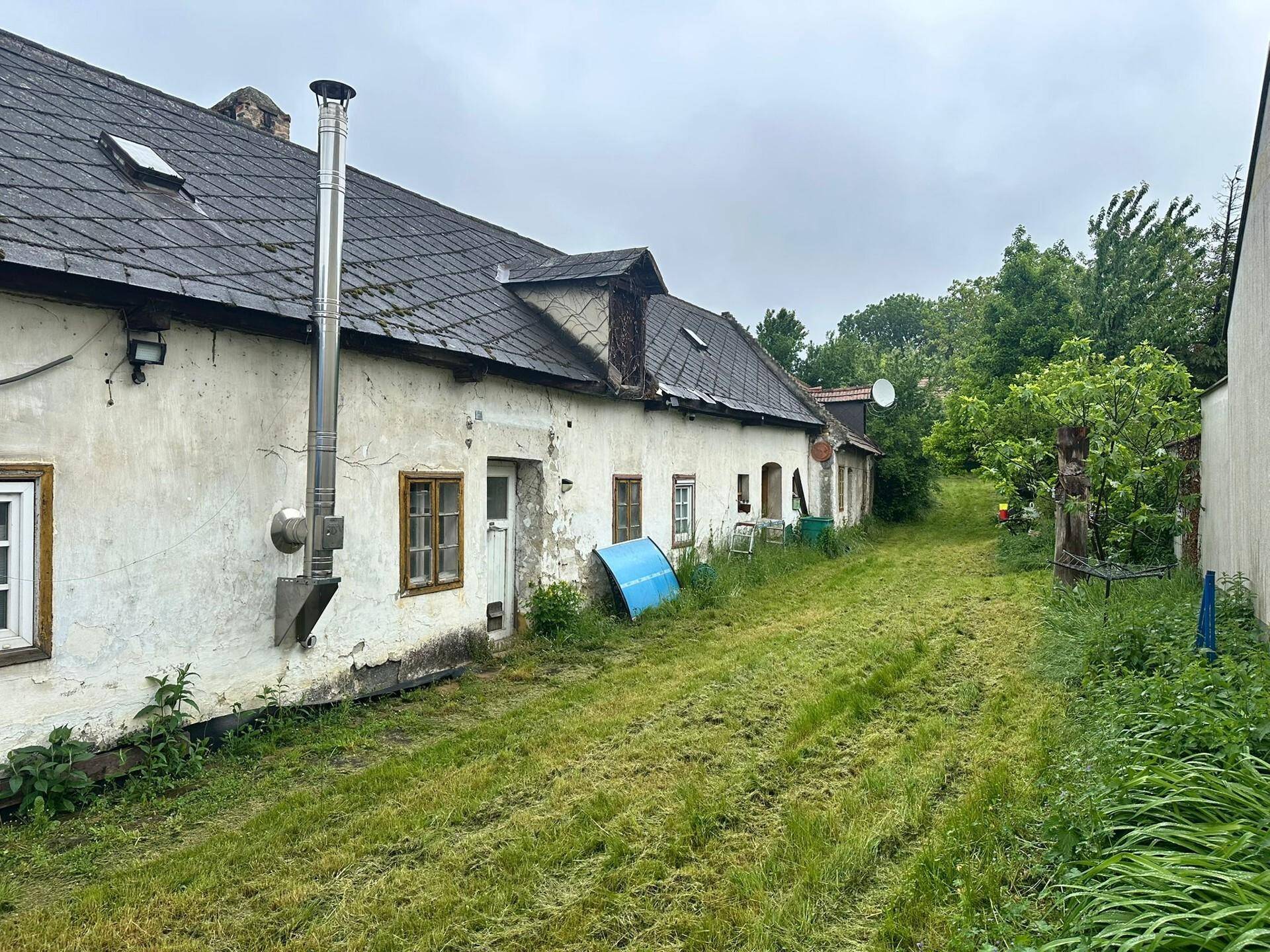 Langes, altes Wohnhaus mit verputzter Fassade und einem weitläufigen, ungepflegten Garten.