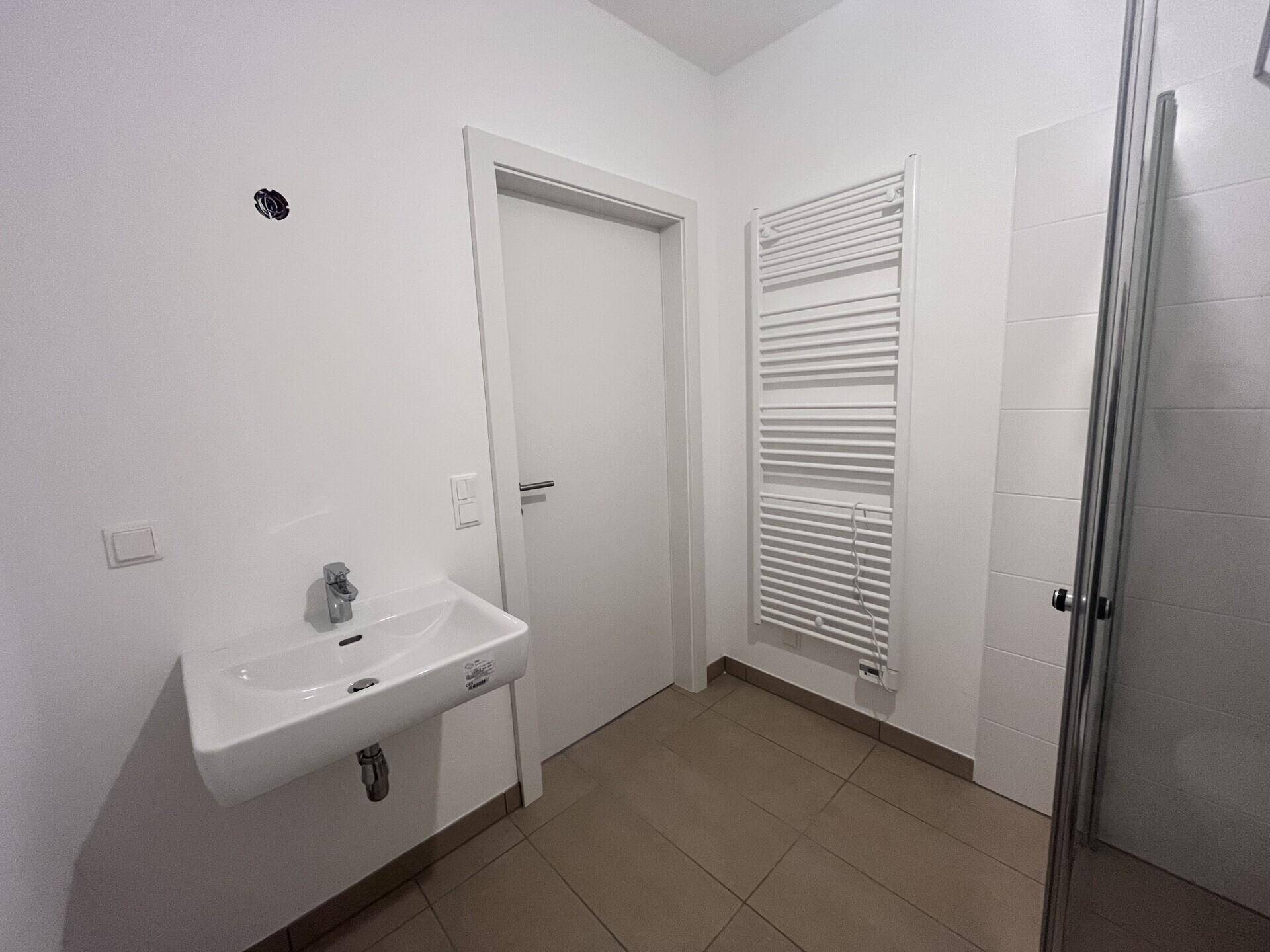 Helles Badezimmer mit Waschbecken, beheiztem Handtuchhalter und weißer Tür.