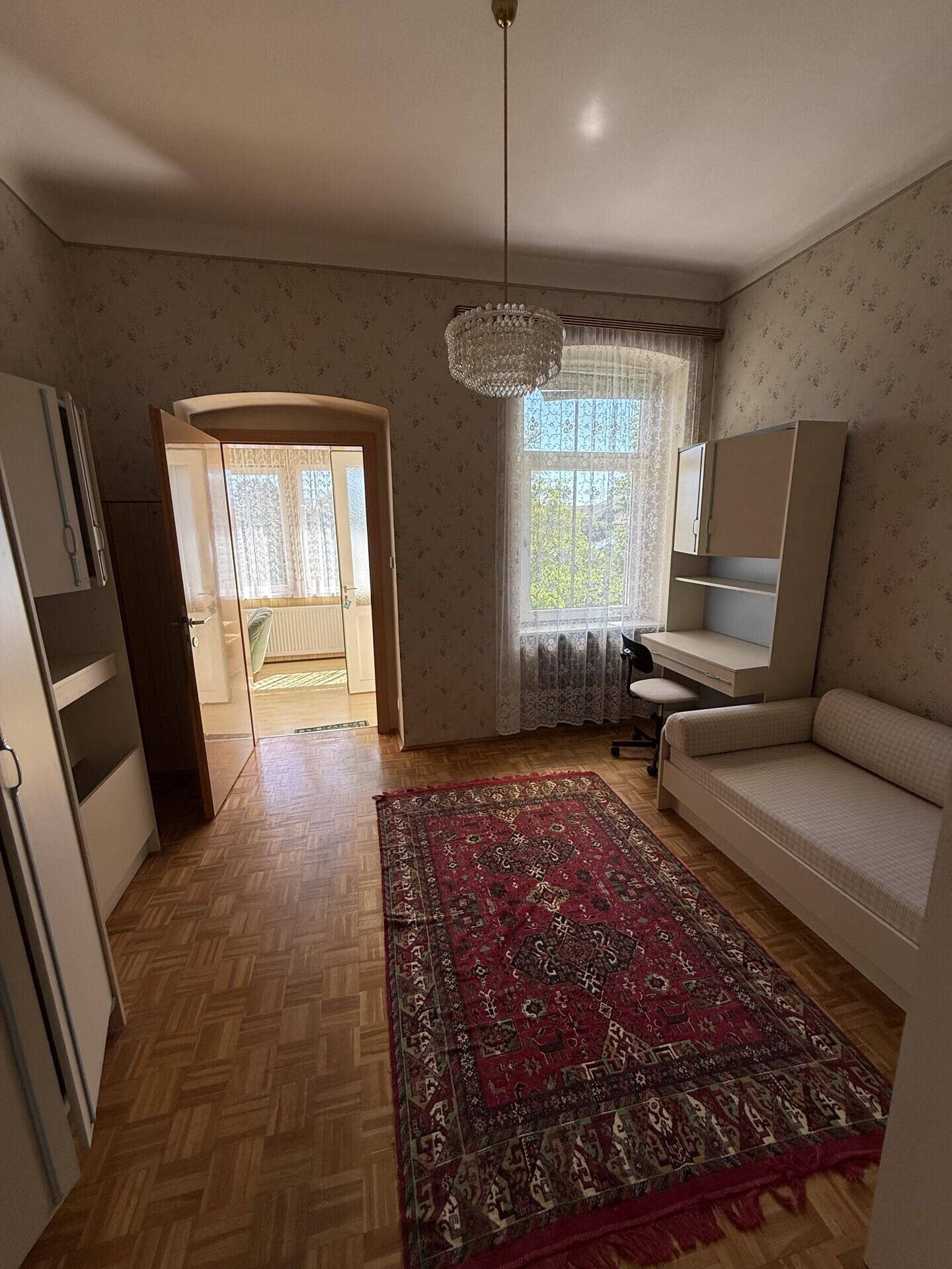 Schlafzimmer mit Parkettboden, Schreibtisch und einem Teppich, der den Raum gemütlich macht.