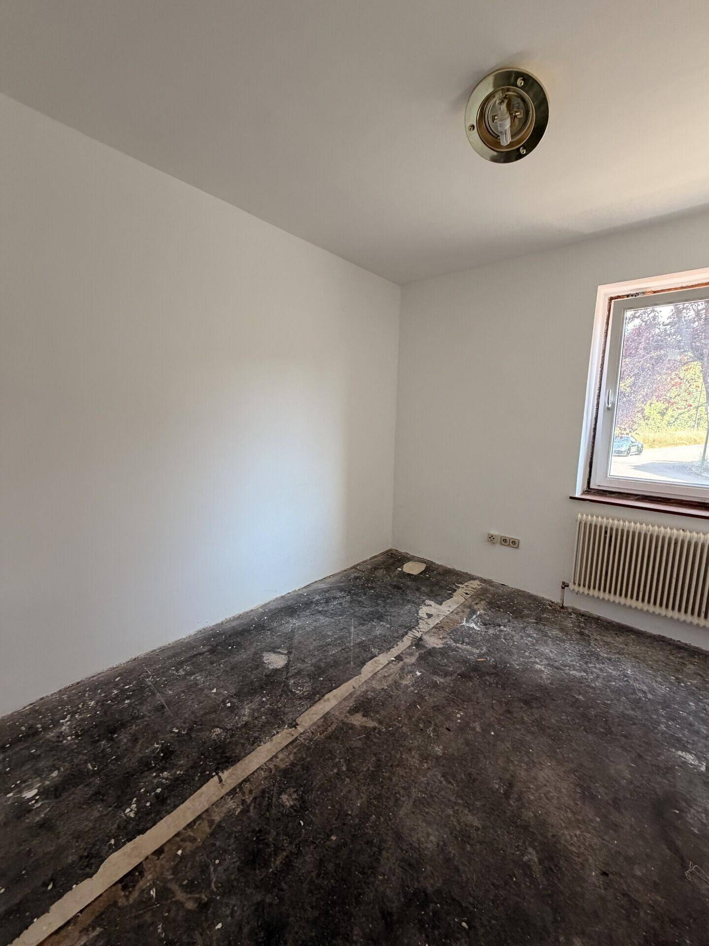 Unmöbliertes Zimmer mit Fenster und Heizung, wartet auf neue Bodenbeläge und Einrichtung.