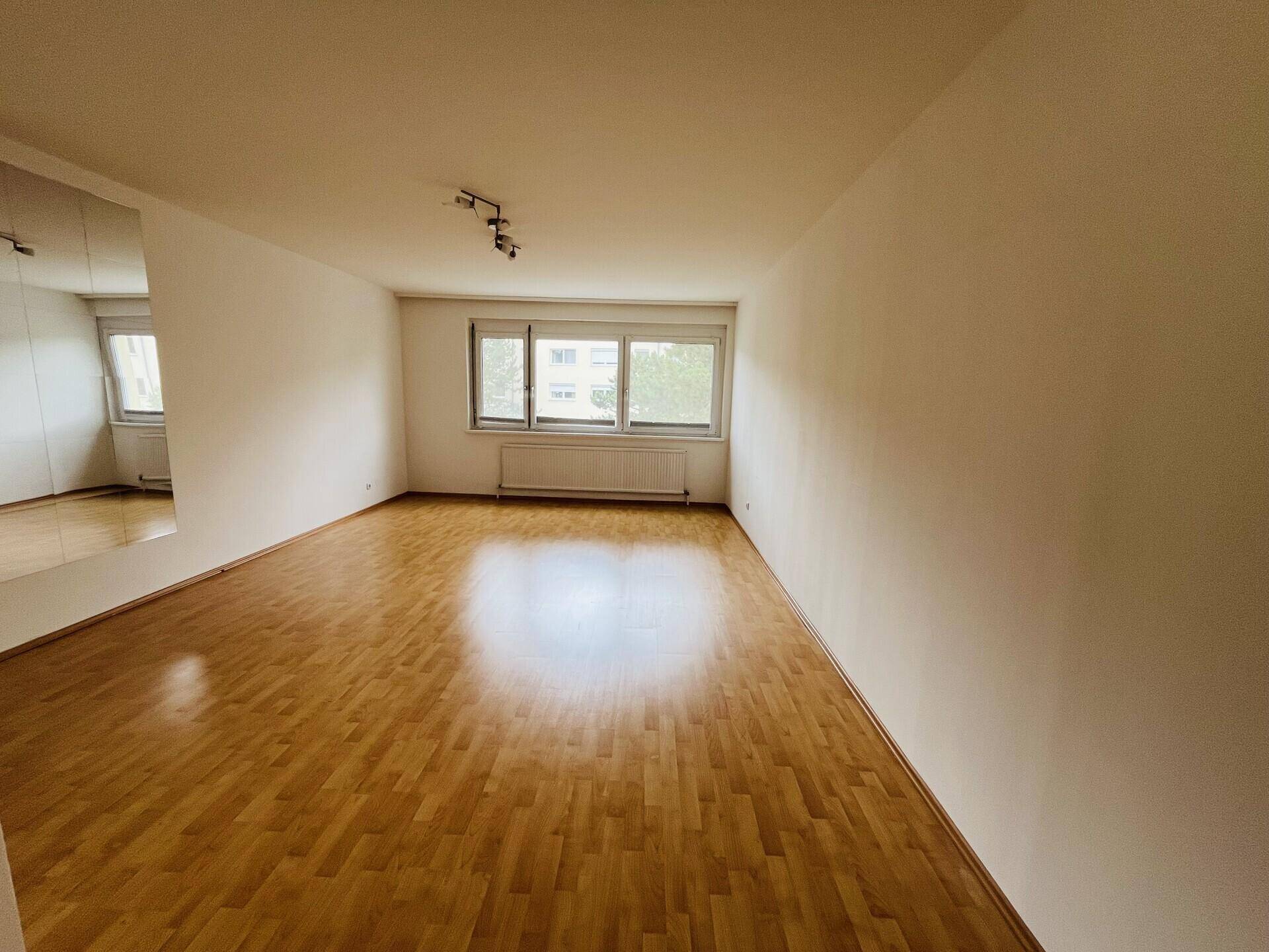 Helles Wohnzimmer mit Parkettboden und großen Fenstern.
