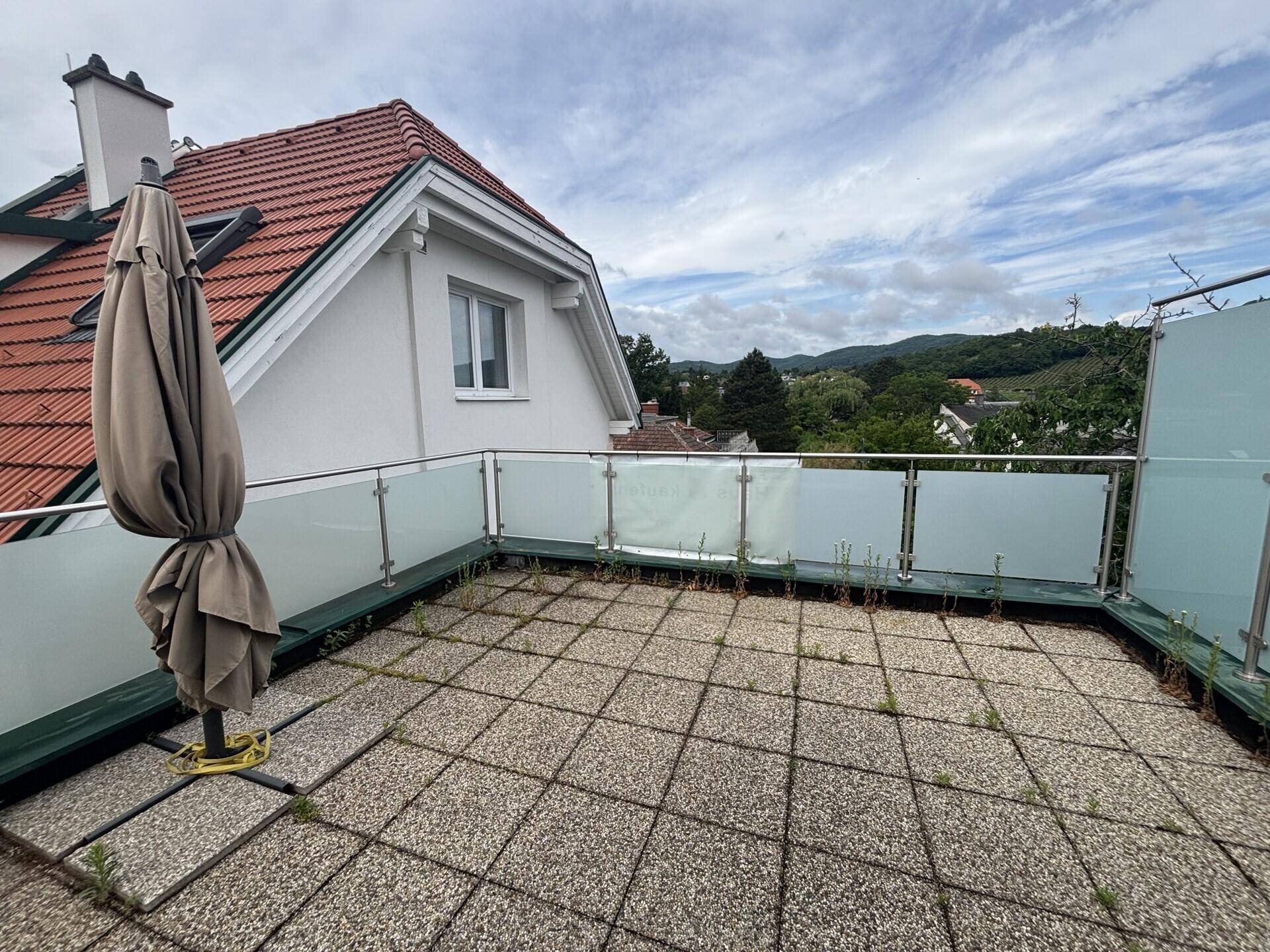 Geräumige Terrasse mit Pflastersteinen, Sonnenschirm und weitem Blick auf die Landschaft.