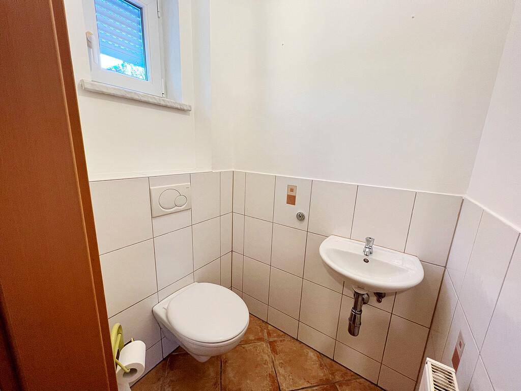 Kleines Gäste-WC mit wandhängender Toilette, Waschbecken und einem Fenster für Tageslicht.