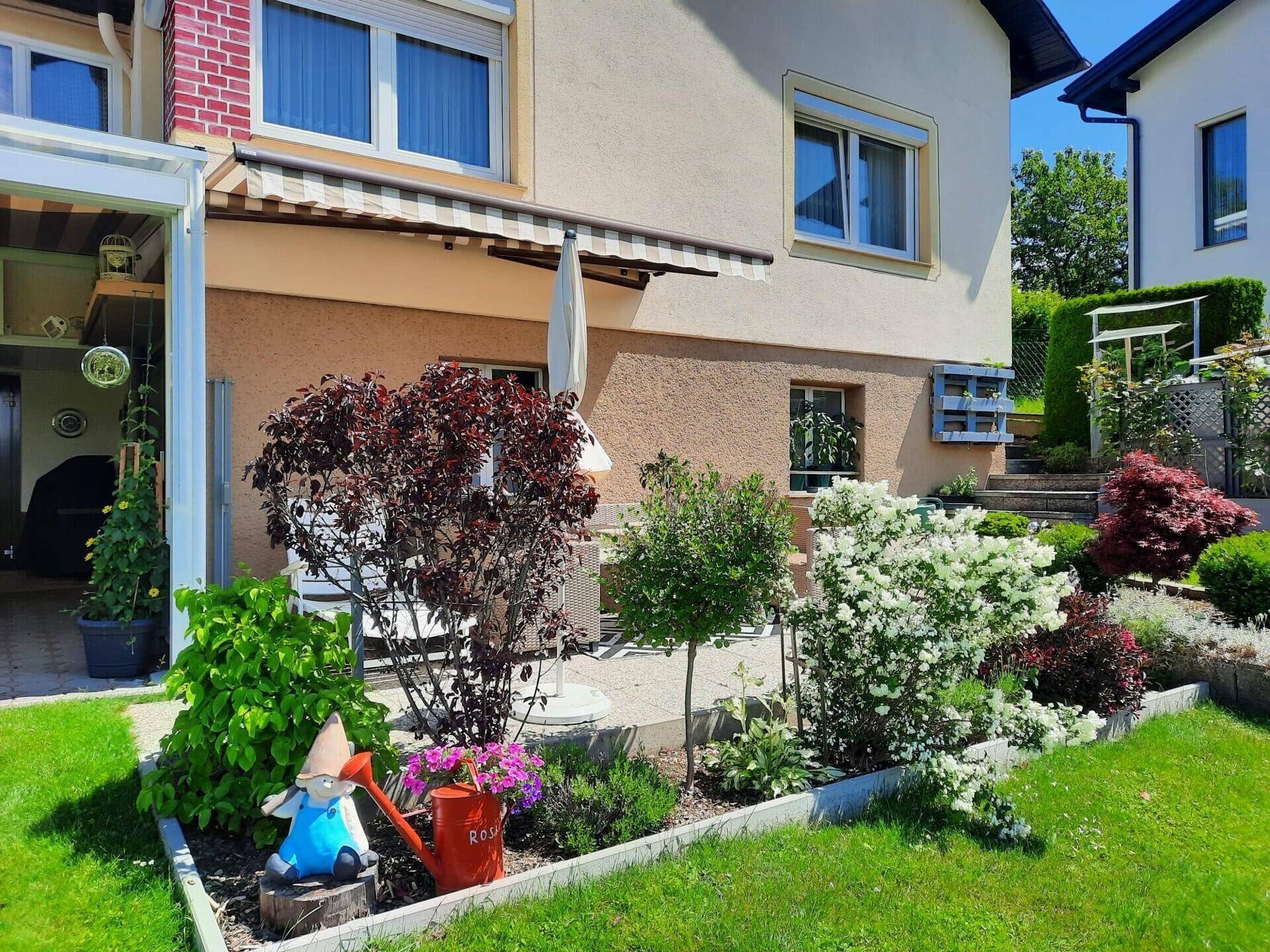Blumenbeet mit Gartenfiguren und verschiedenen Pflanzen neben der Terrasse.