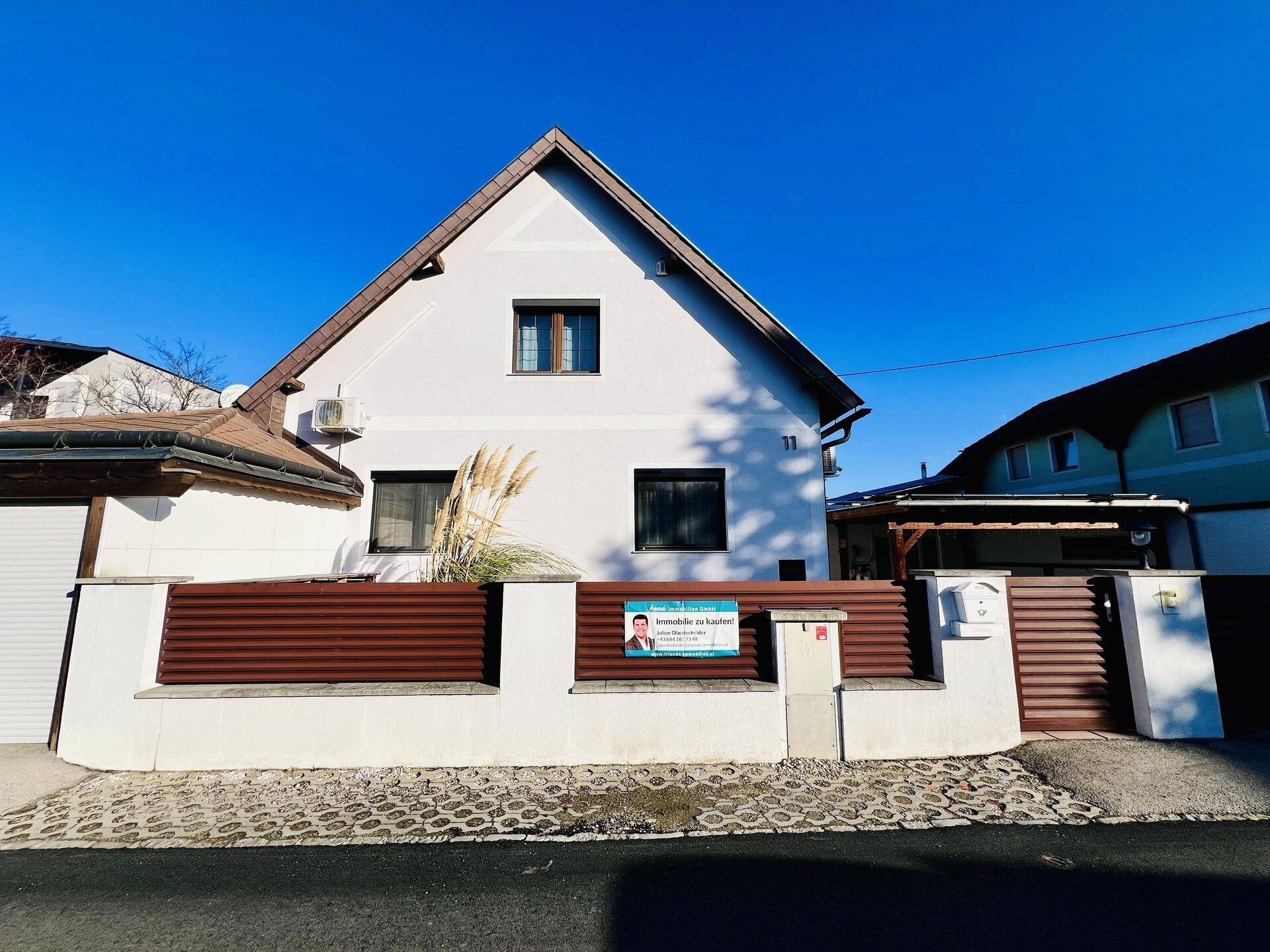 Ansicht der Hausfassade von der Straße aus mit einem Immobilien-Werbeschild am Zaun.