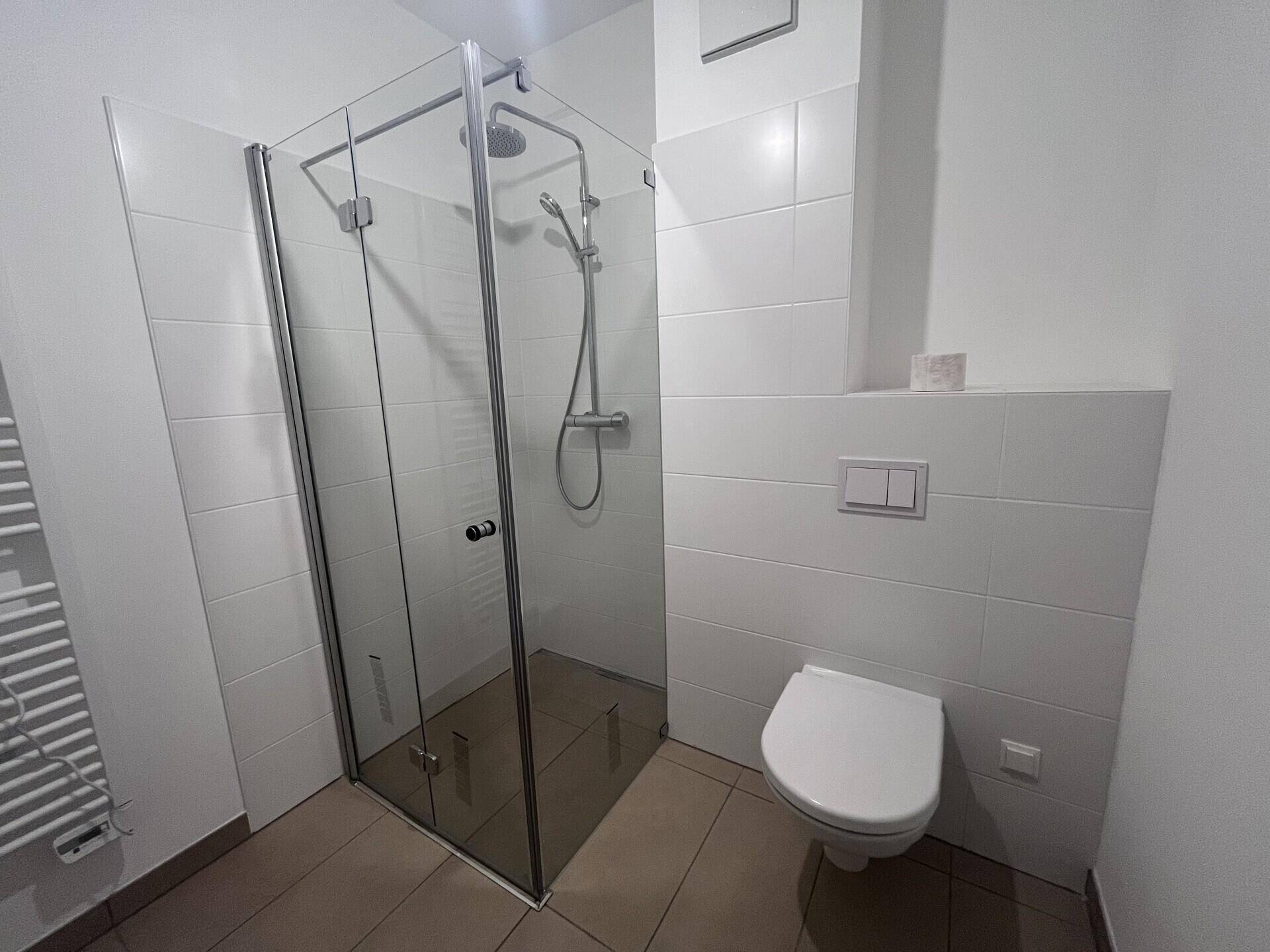 Modernes Badezimmer mit Duschkabine, wandhängendem WC und hellen Fliesen.