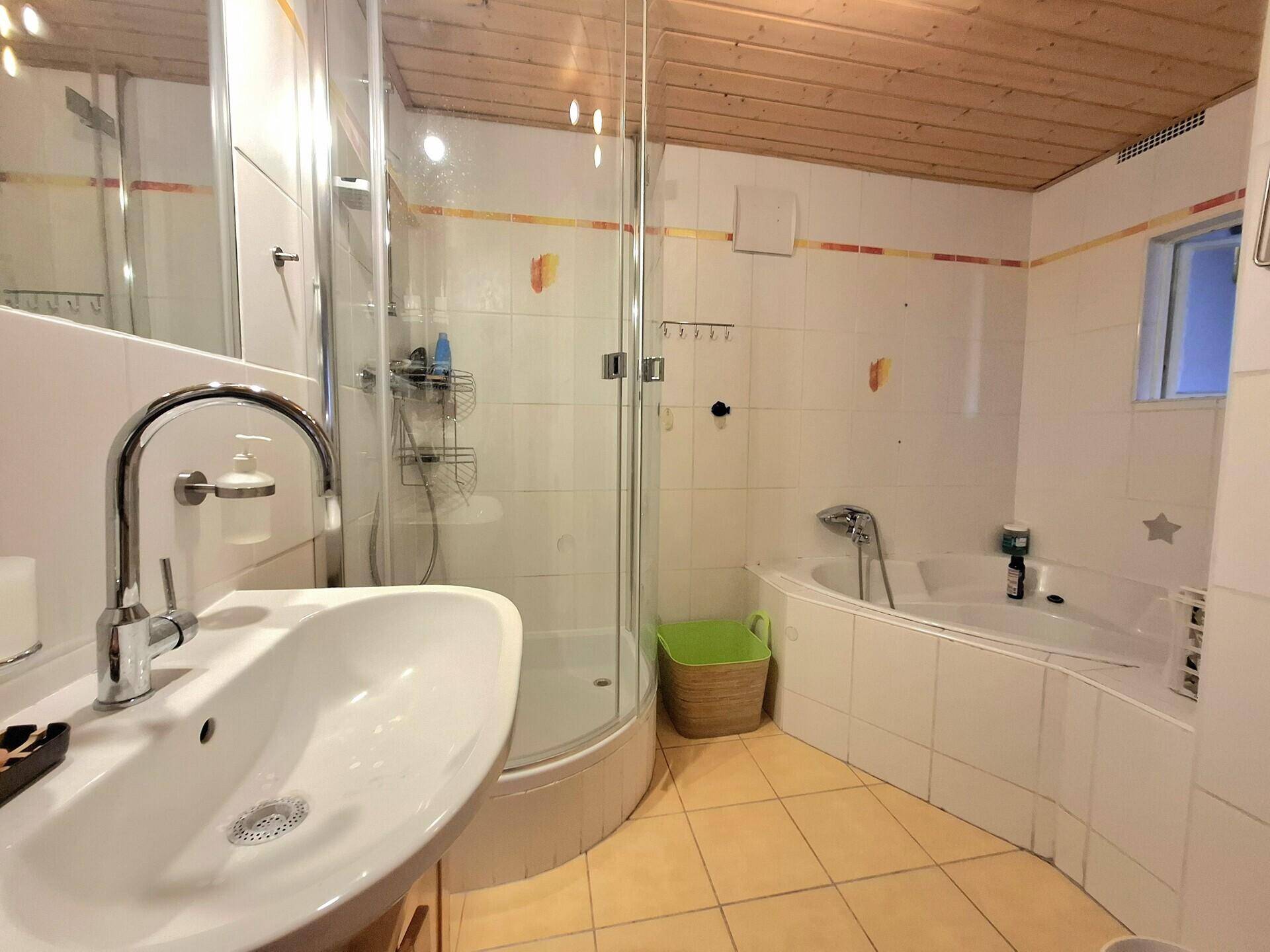 Badezimmer mit Eckbadewanne, Duschkabine und Holzdecke, ausgestattet mit gelben Akzenten.