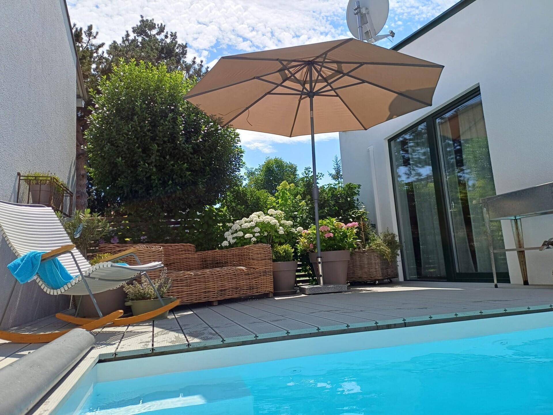 Sonniger Terrassenbereich mit kleinem Pool, bequemen Loungemöbeln und großem Sonnenschirm.