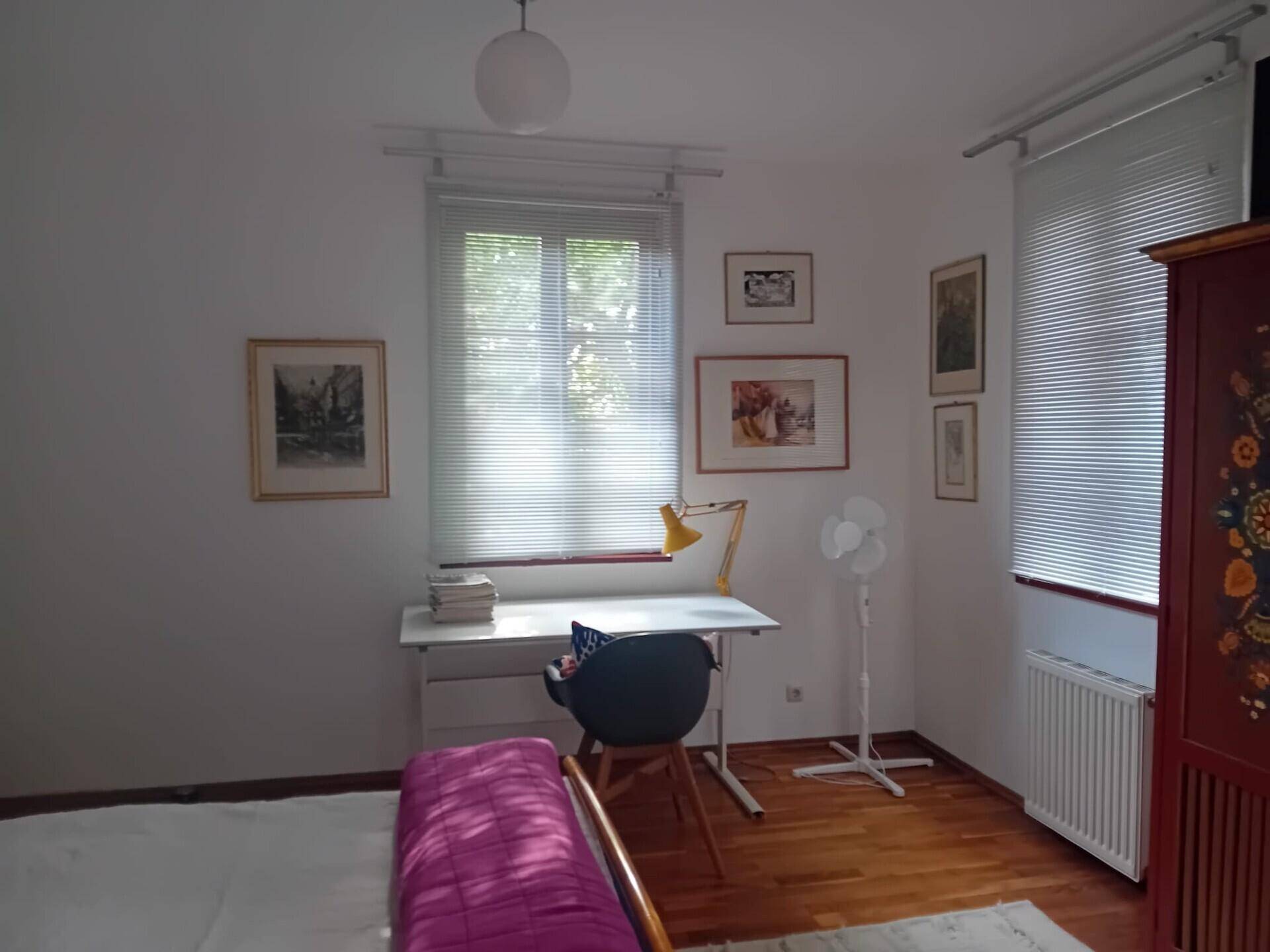 Helles Schlafzimmer mit Schreibtisch, Fenster und farbenfrohem Schrank, Holzboden.