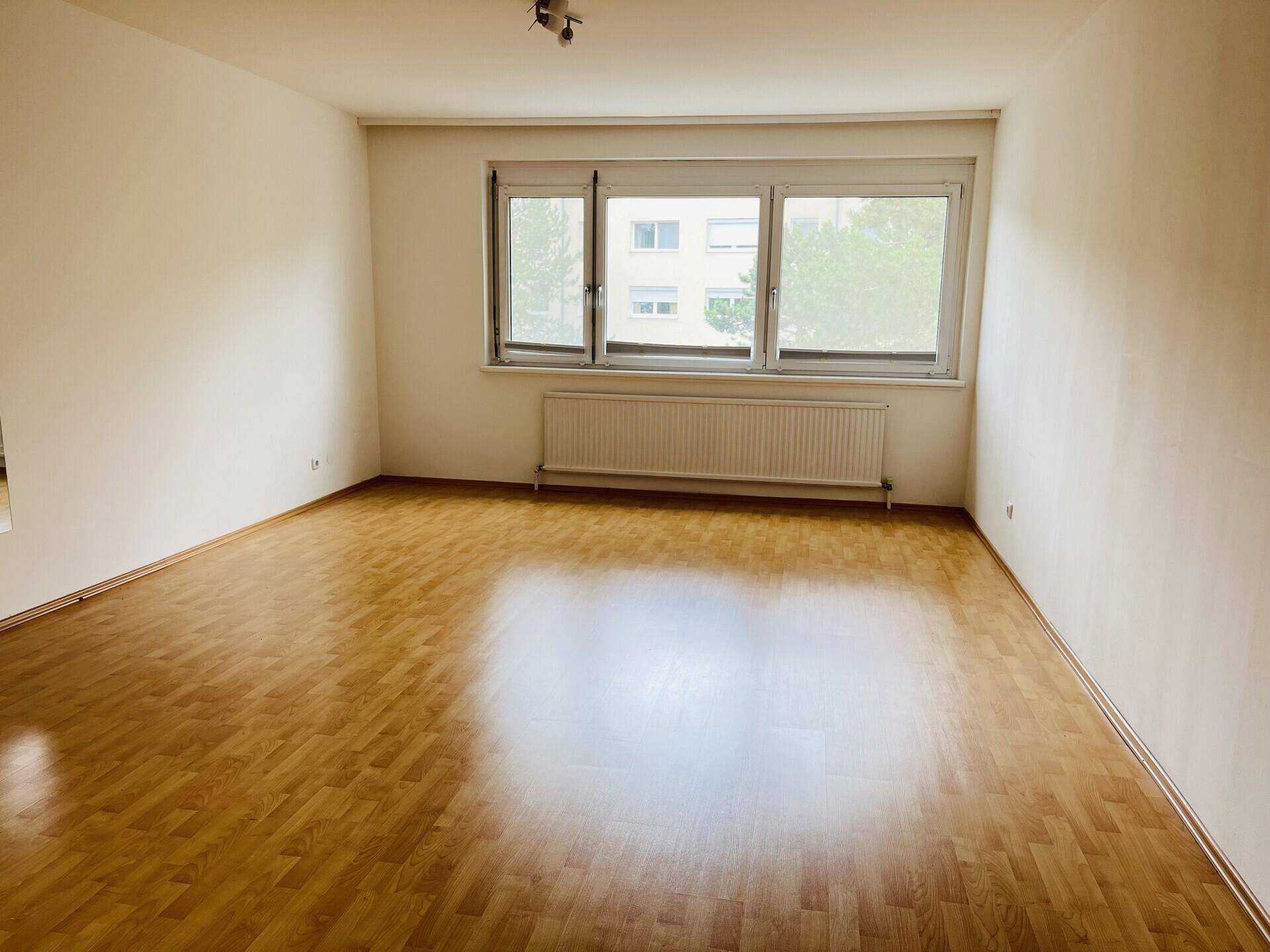 Geräumiges Wohnzimmer mit Parkettboden und Blick ins Grüne.