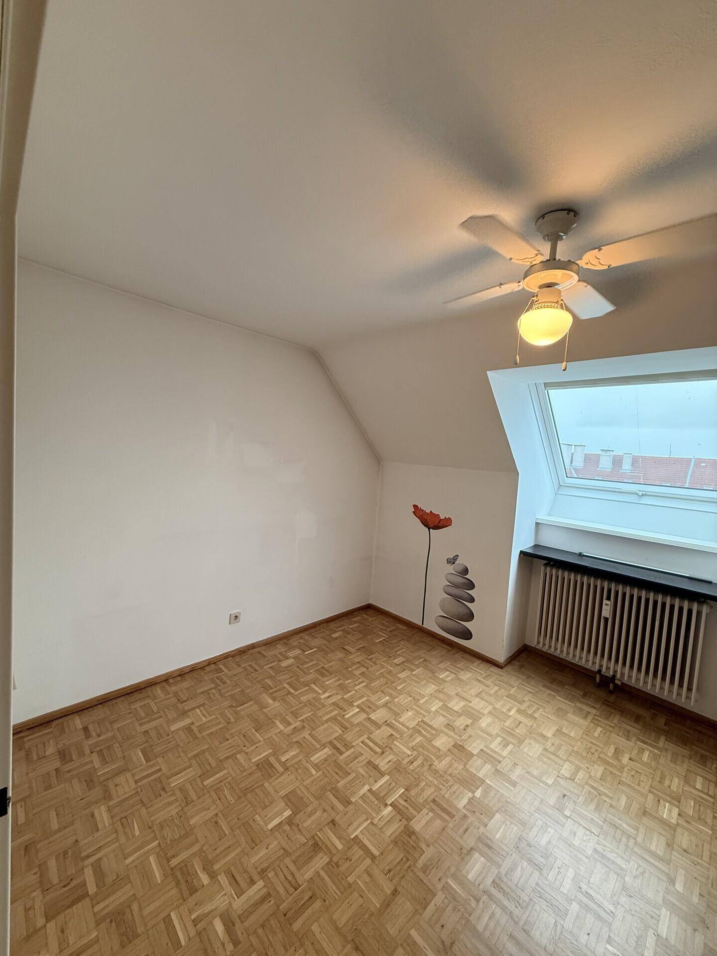Leeres Schlafzimmer mit Dachschräge, Parkettboden und Dachfenster, bereit zur Einrichtung.