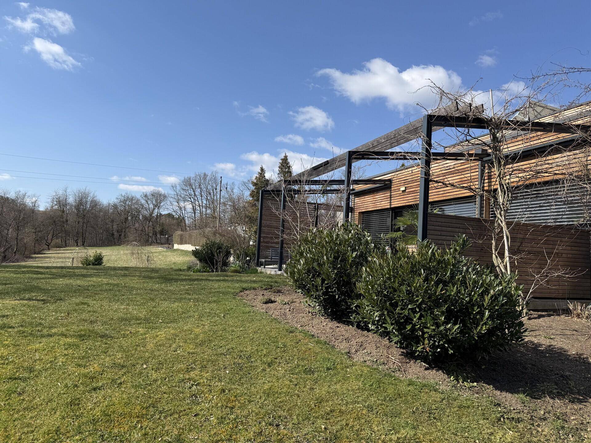 Seitenansicht des modernen Hauses mit Holzfassade und weitläufiger Rasenfläche unter blauem Himmel.