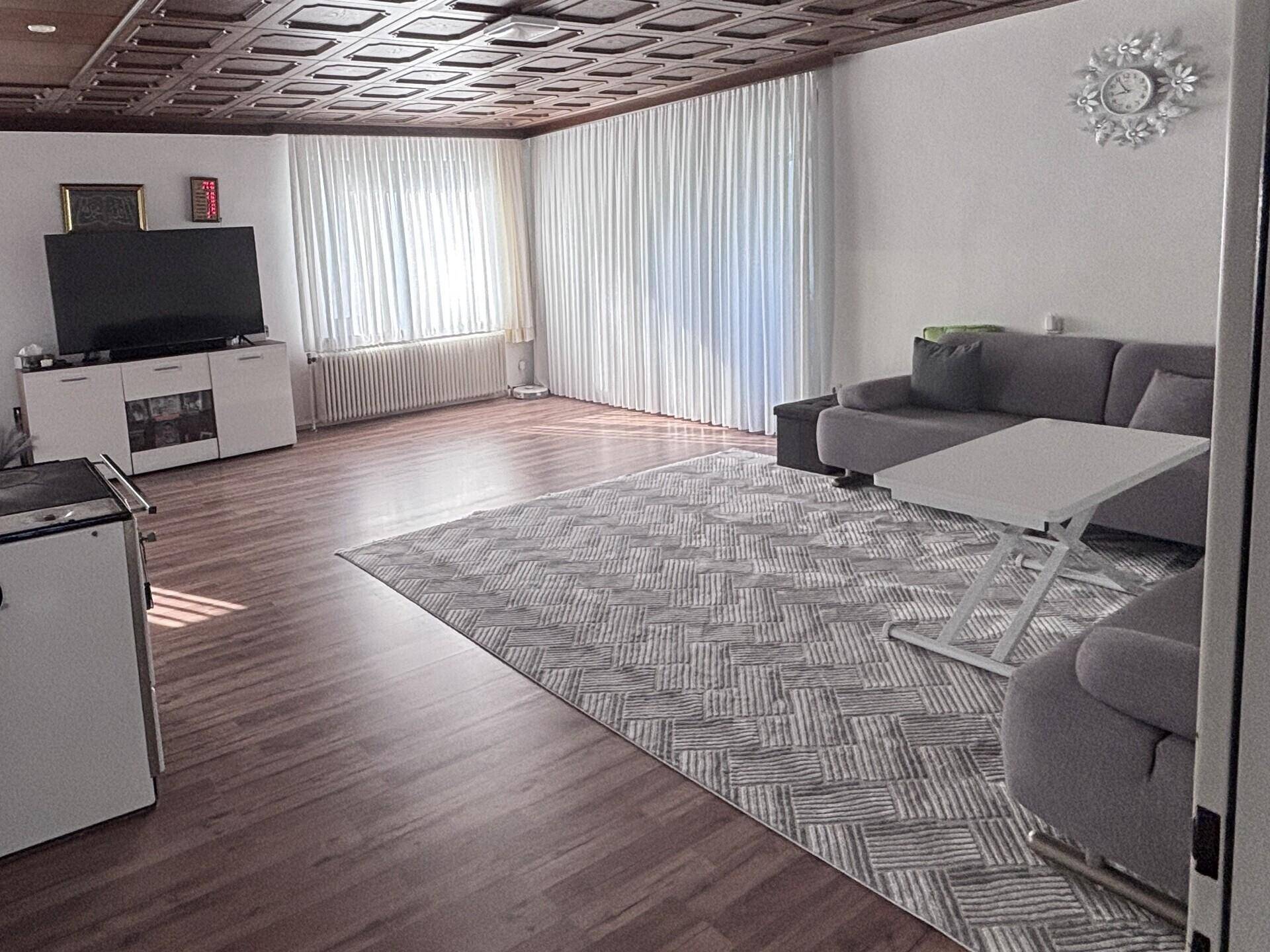 Helles Wohnzimmer mit Holzboden, großem Fenster und dekorativer Kassettendecke.