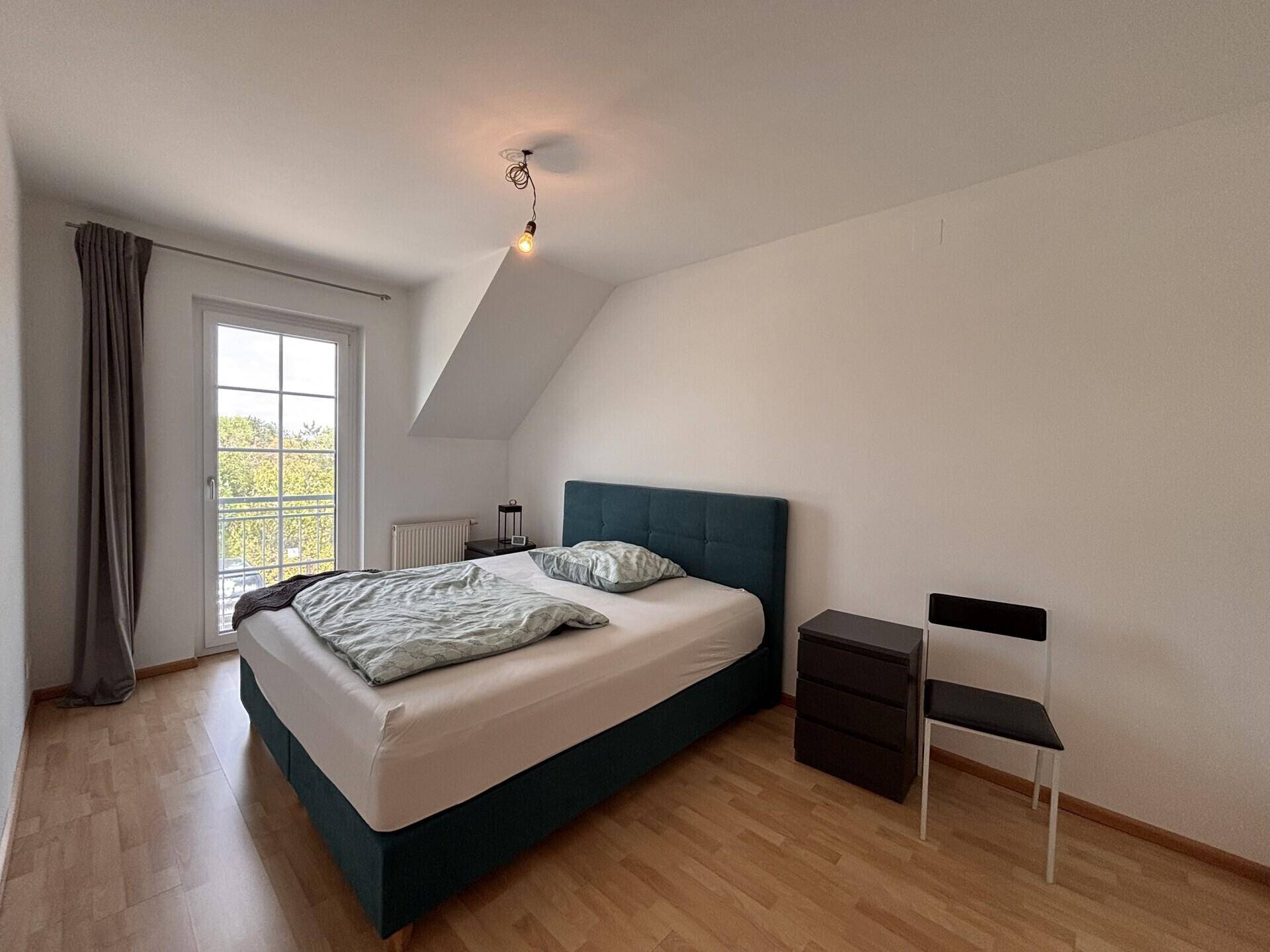 Schlafzimmer mit teal-farbenem Bett, Nachtschrank und Zugang zu einem französischen Balkon.