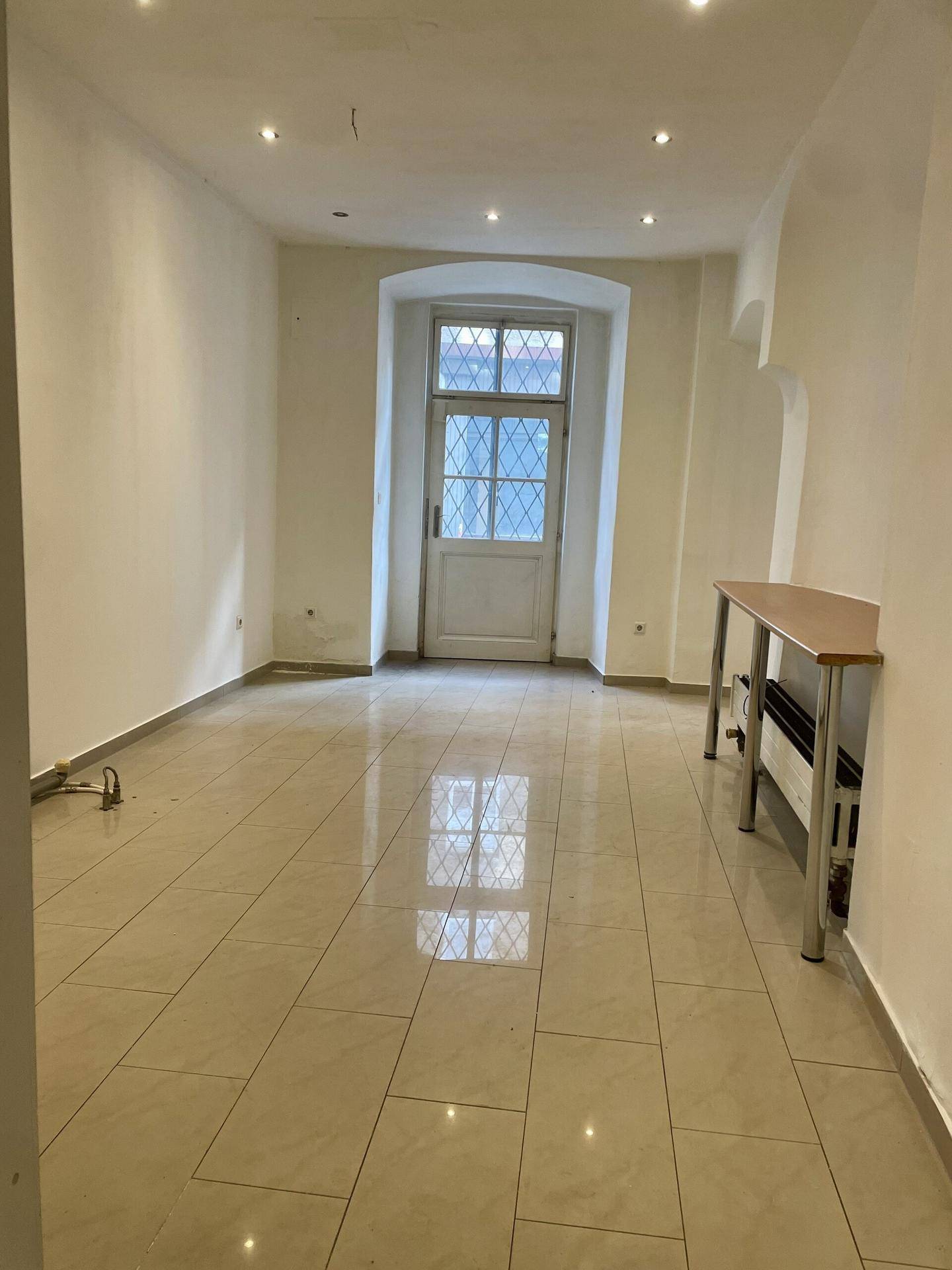 Heller, leerer Raum mit Fliesenboden und einem Fenster mit Sprossen, das Tageslicht hereinlässt.