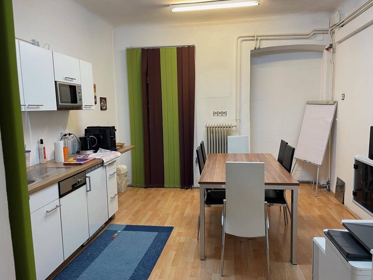 Funktionale Küche mit weißen Schränken, Esstisch und Stühlen, ideal für Pausen im Büro.