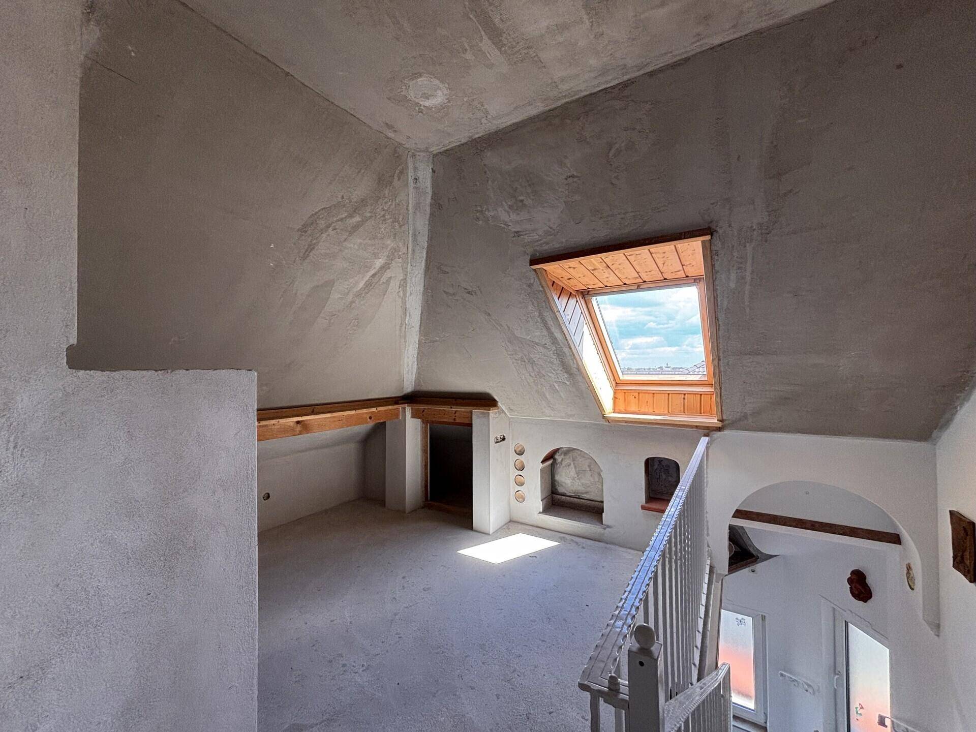 Dachgeschoss-Treppenbereich im Rohbau mit Dachfenster und unfertigen Wänden.