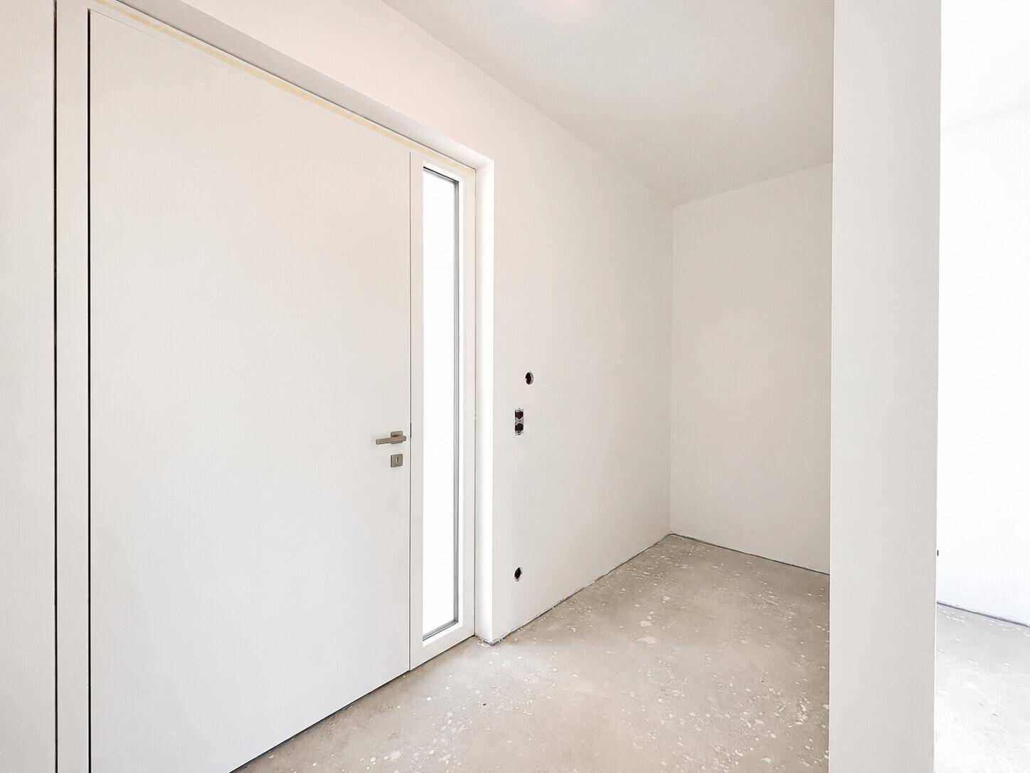 Unfertiger Eingangsbereich mit weißer Tür und Betonboden, bereit für den weiteren Ausbau.