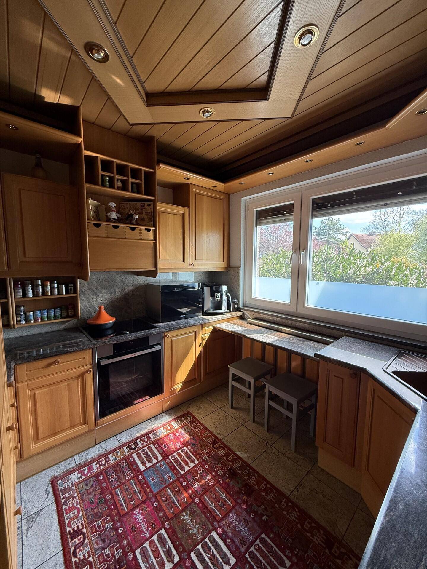 Traditionelle Holzküche mit Einbaugeräten, Fenster und gemustertem Teppich.